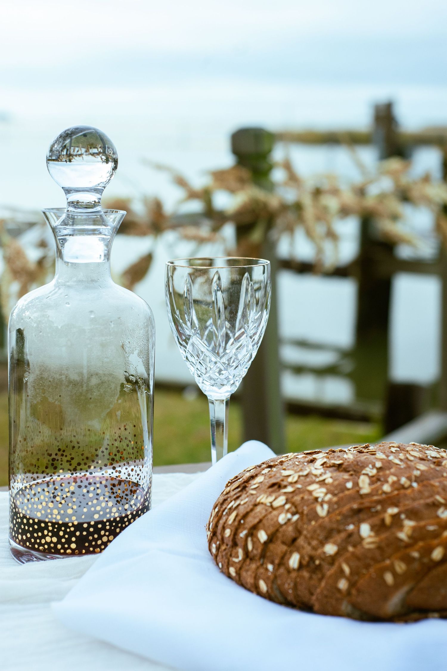 Crystal decanter and glasses arranged with rustic bread on white tablecloth.