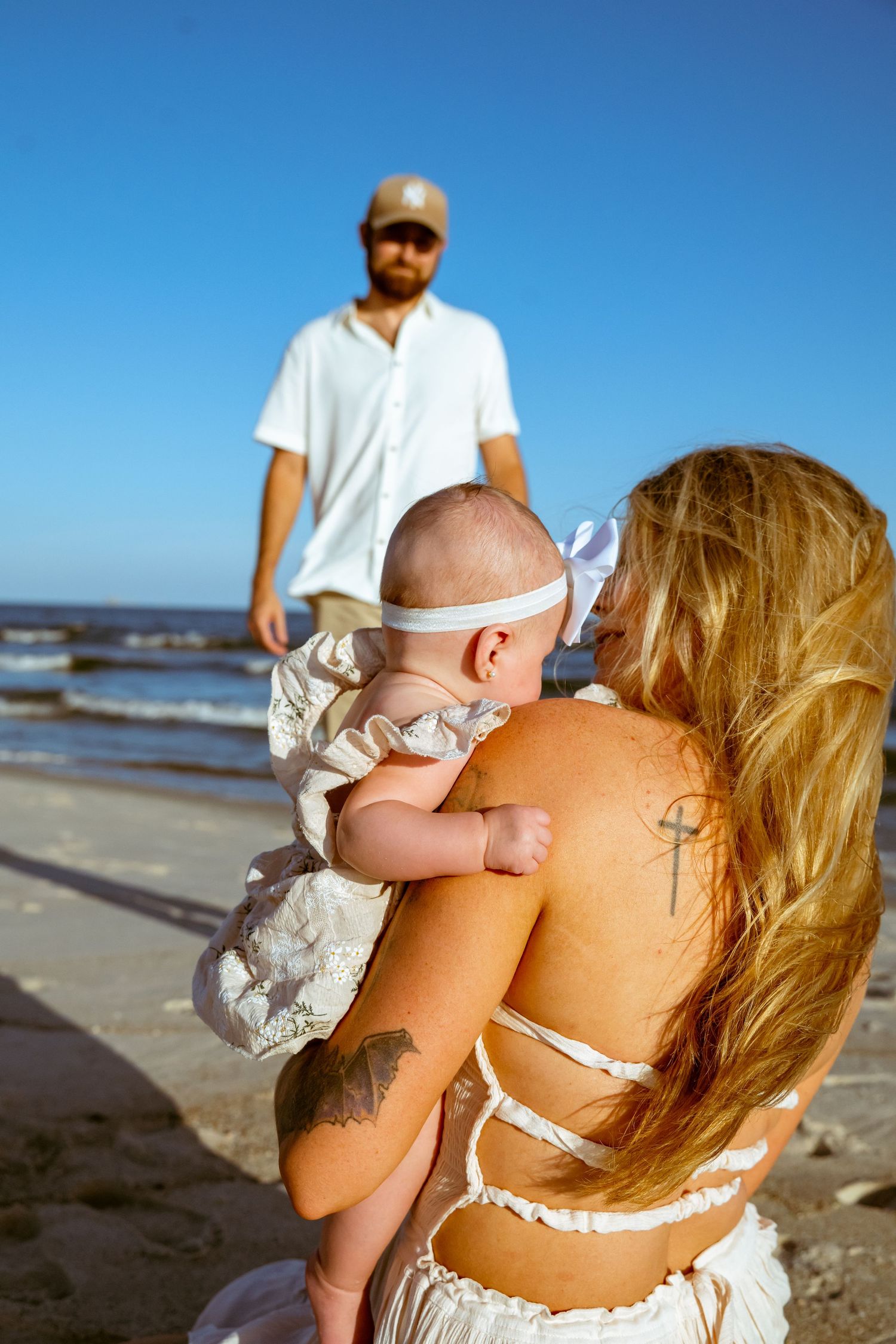 A family playing with an infant on a sunny beach during golden hour.
