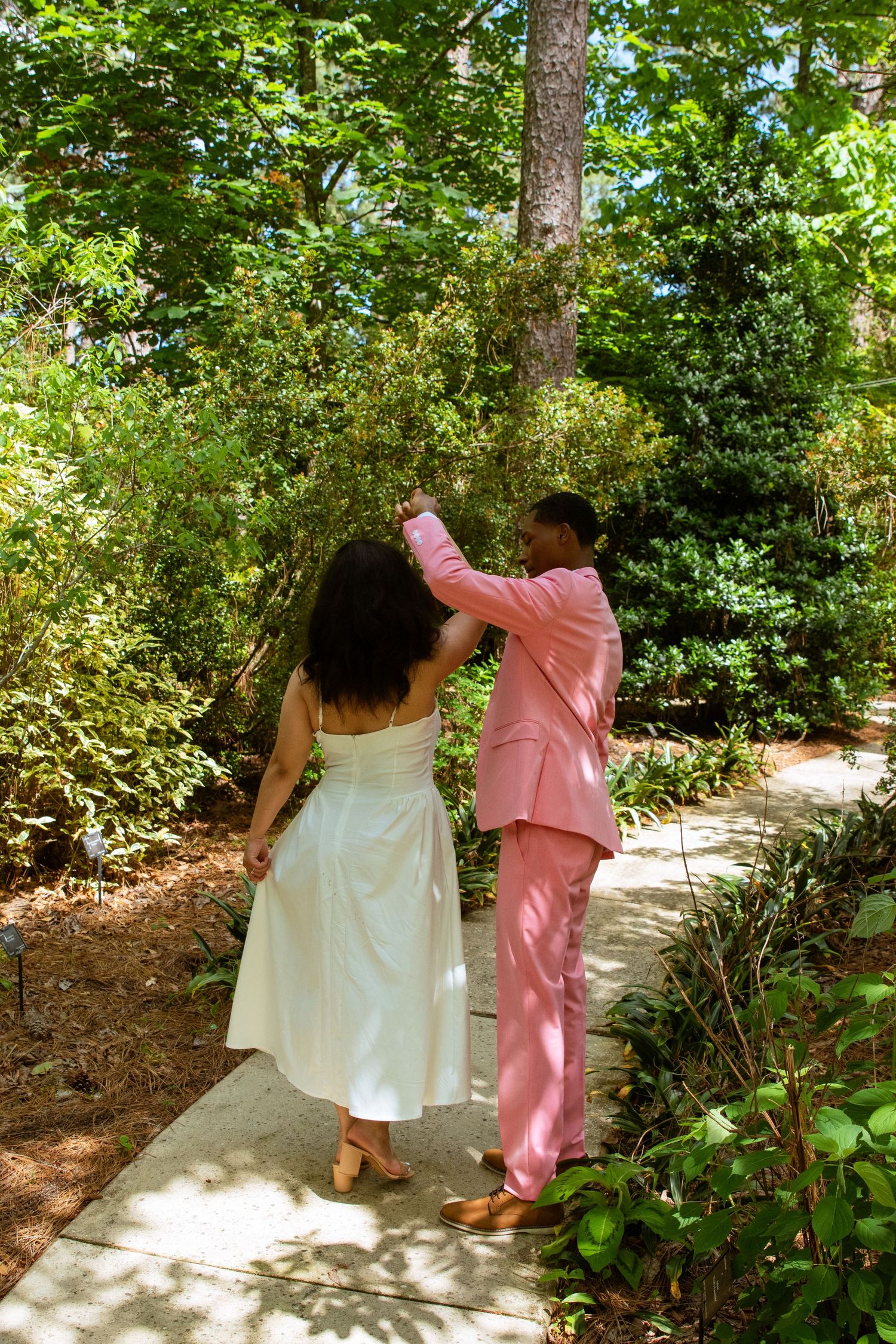 A couple dances along a garden path, with the person in pink leading.