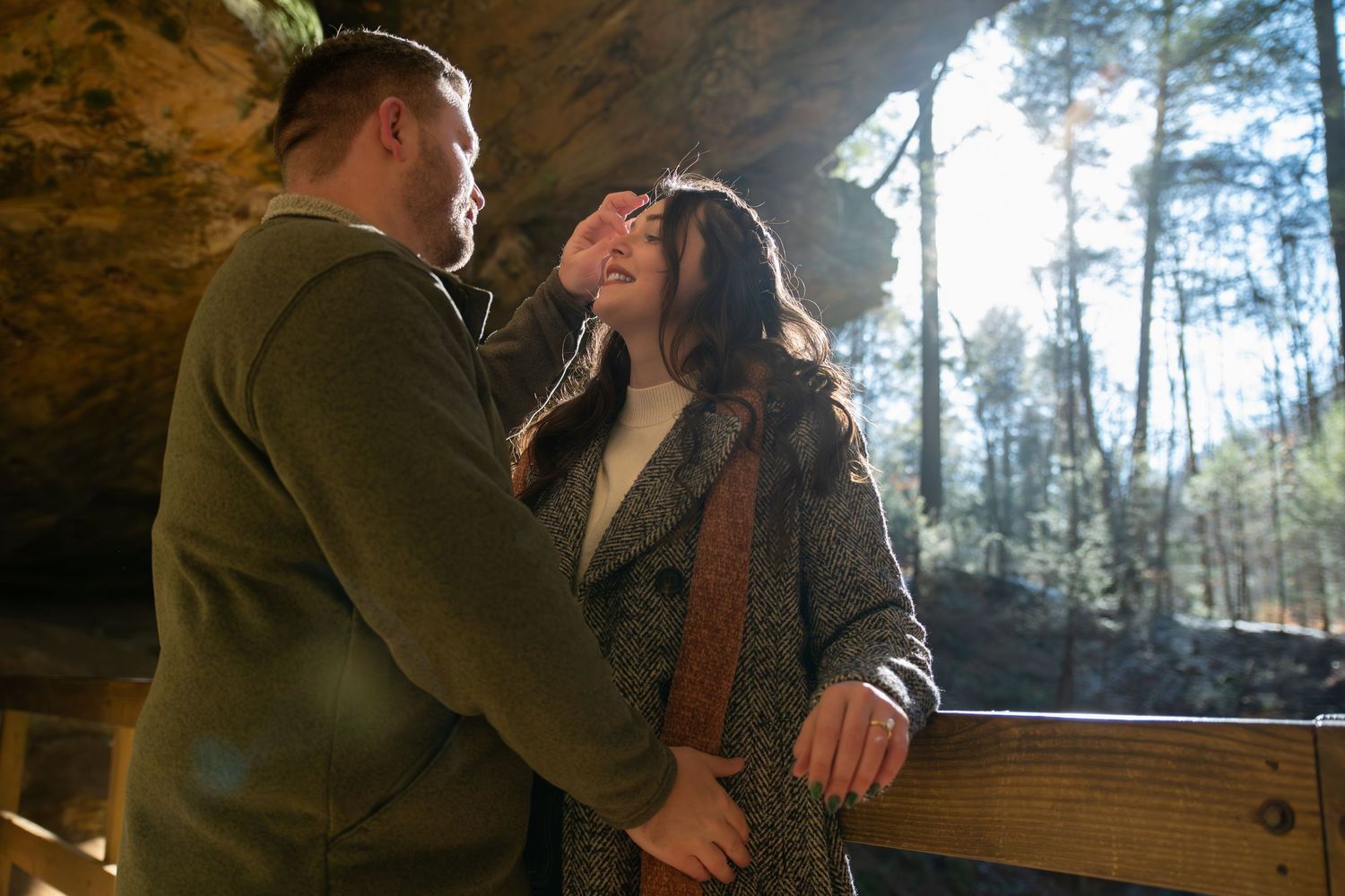 A couple shares intimate moments in a cozy cabin setting surrounded by forest views through large windows.