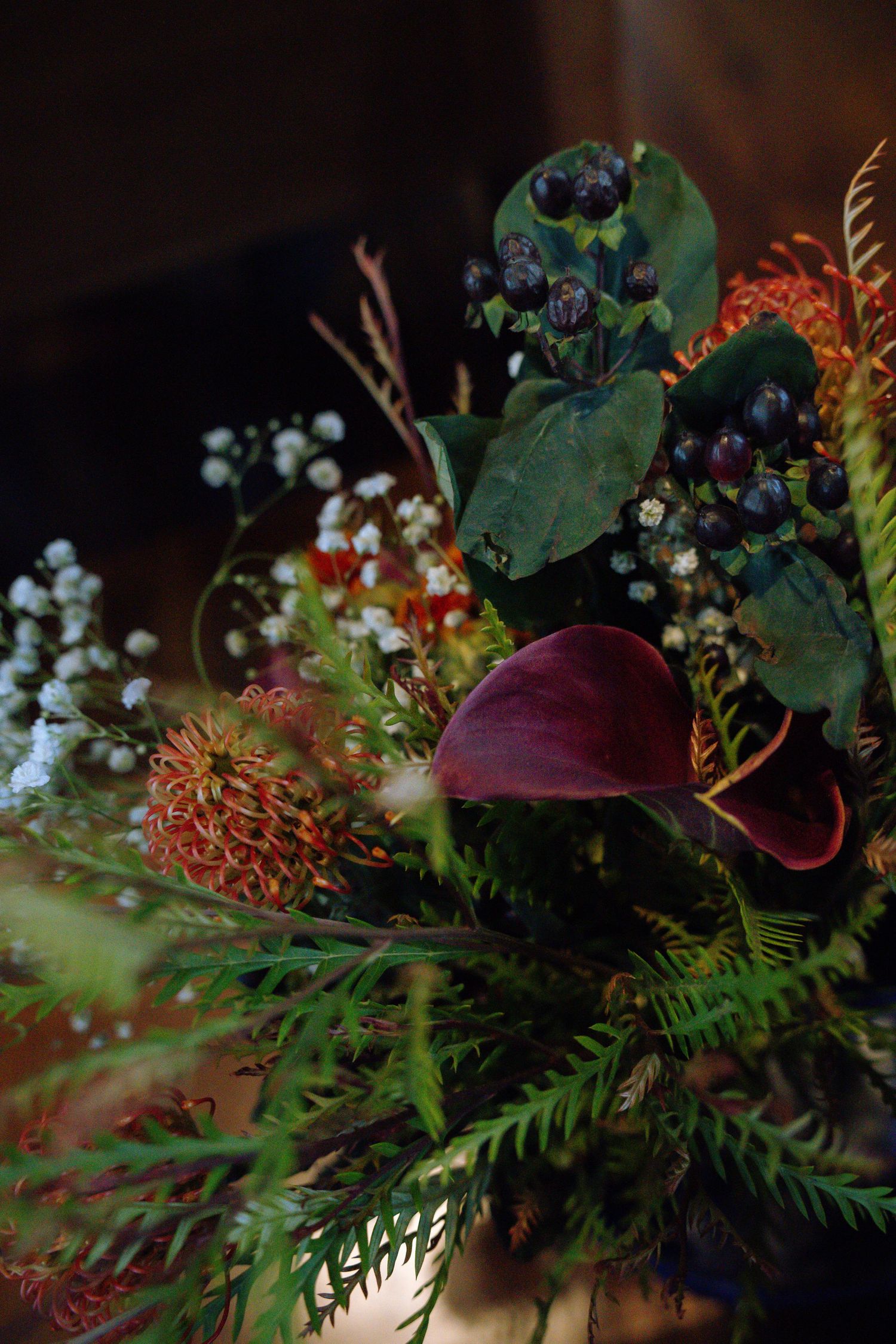An elegant floral arrangement featuring dark foliage, burgundy calla lilies, and baby's breath.