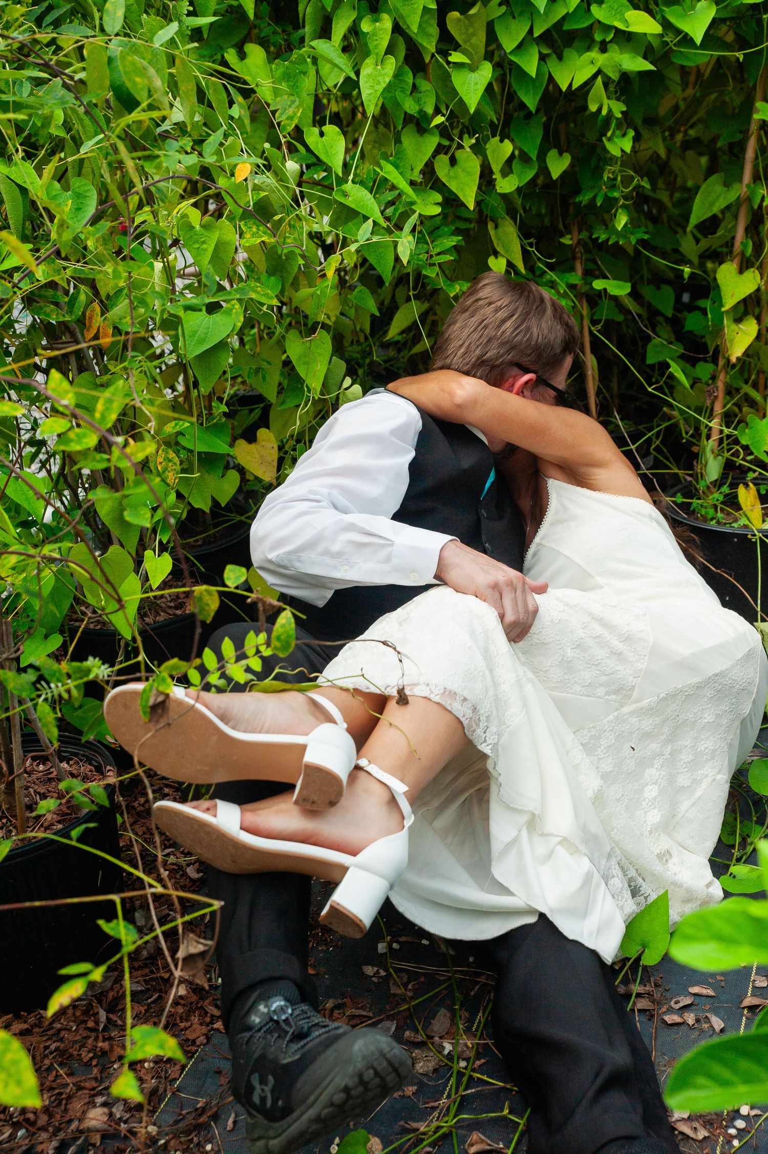 Wedding attire-clad couple shares a romantic moment among lush green foliage in garden setting.