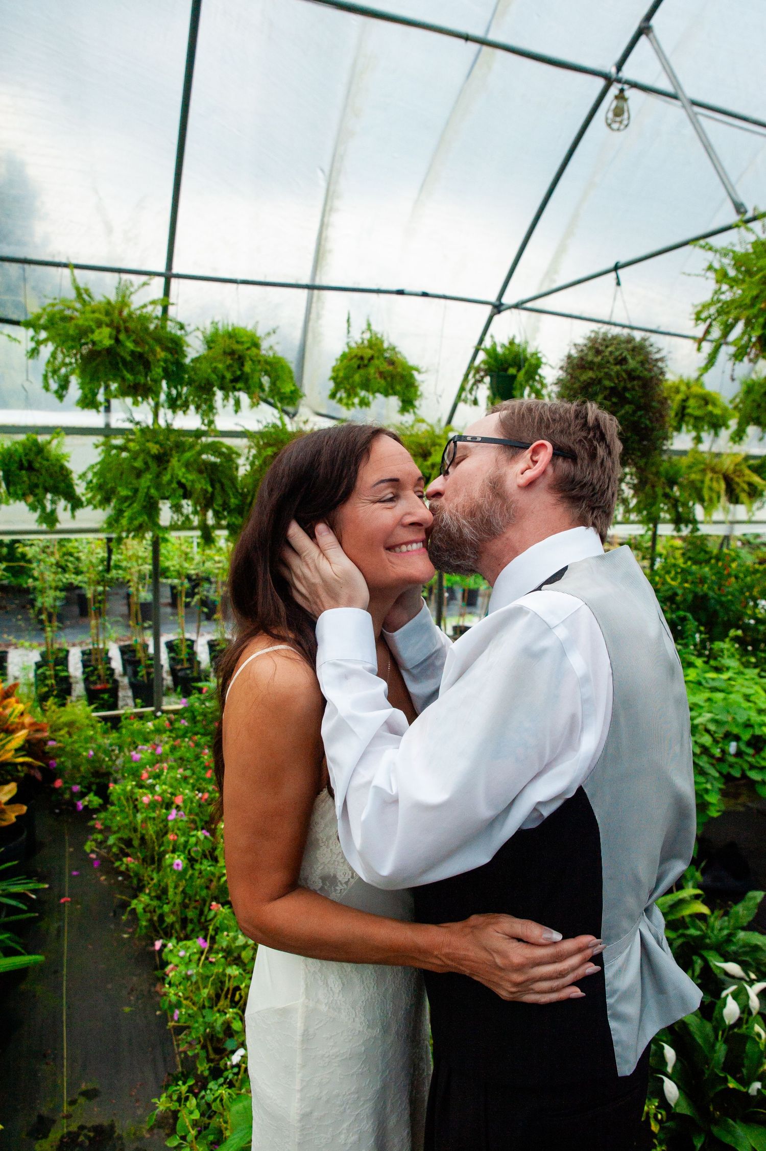 Romantic moment in a greenhouse with loving embrace surrounded by lush greenery and plants.