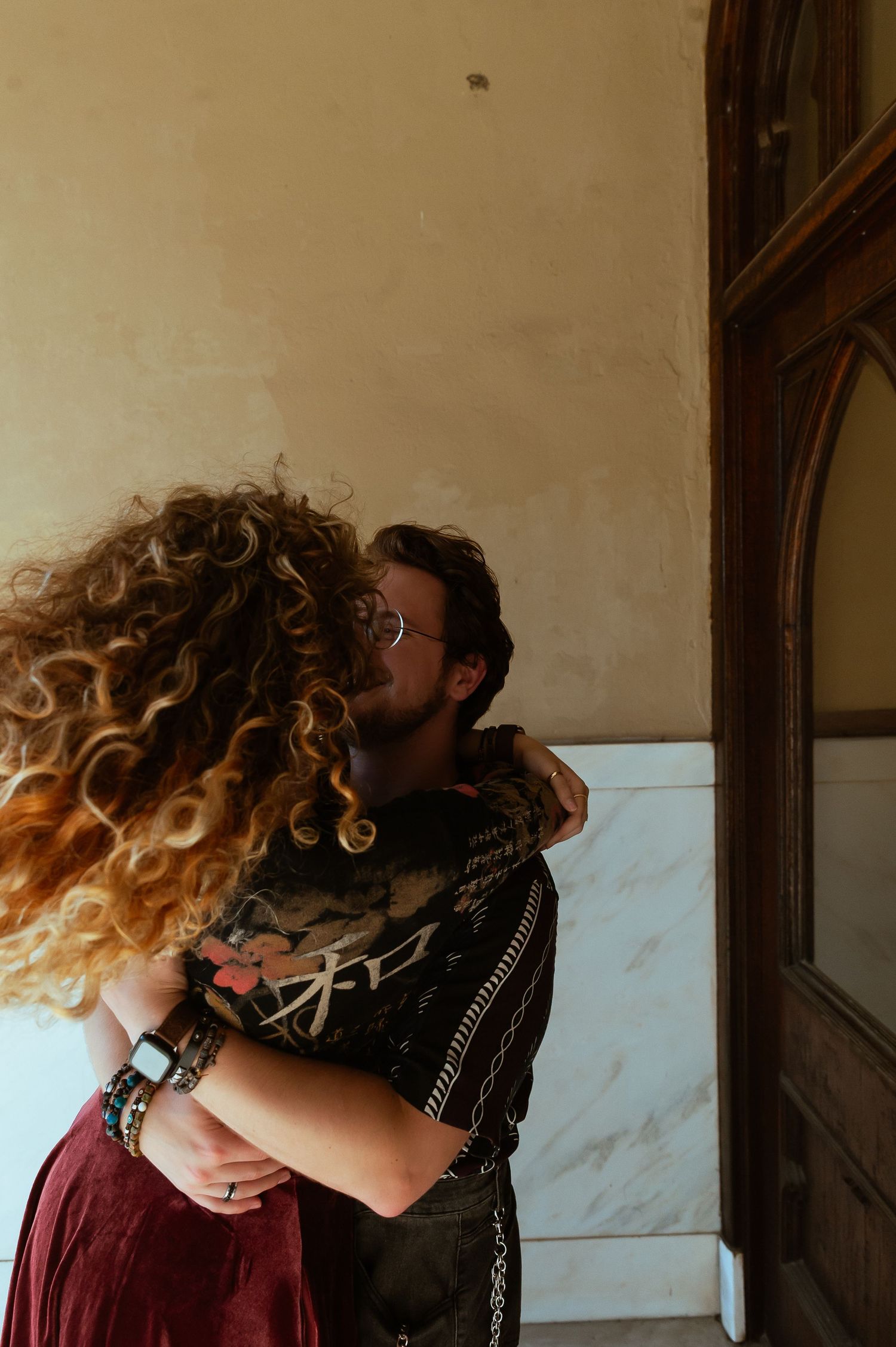 Two people in stylish outfits leaning in close together against a marble wall in moody indoor lighting.