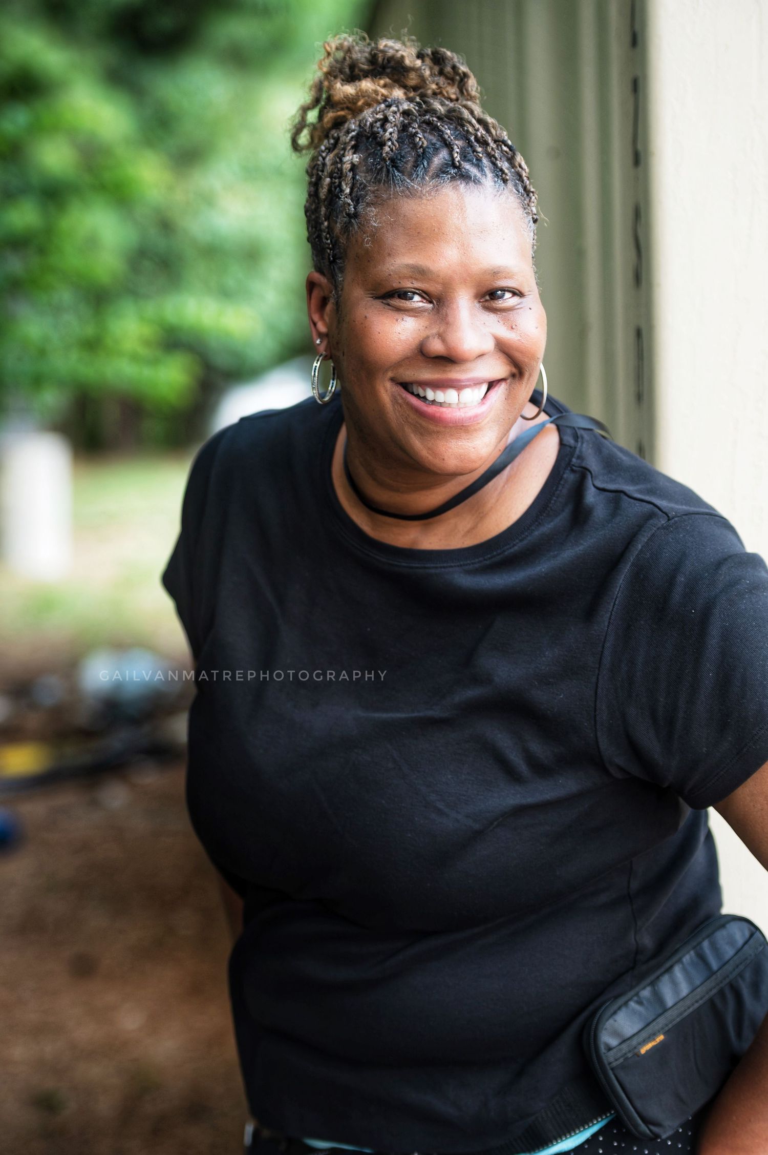 Person in black shirt smiling warmly in outdoor portrait series with natural lighting.