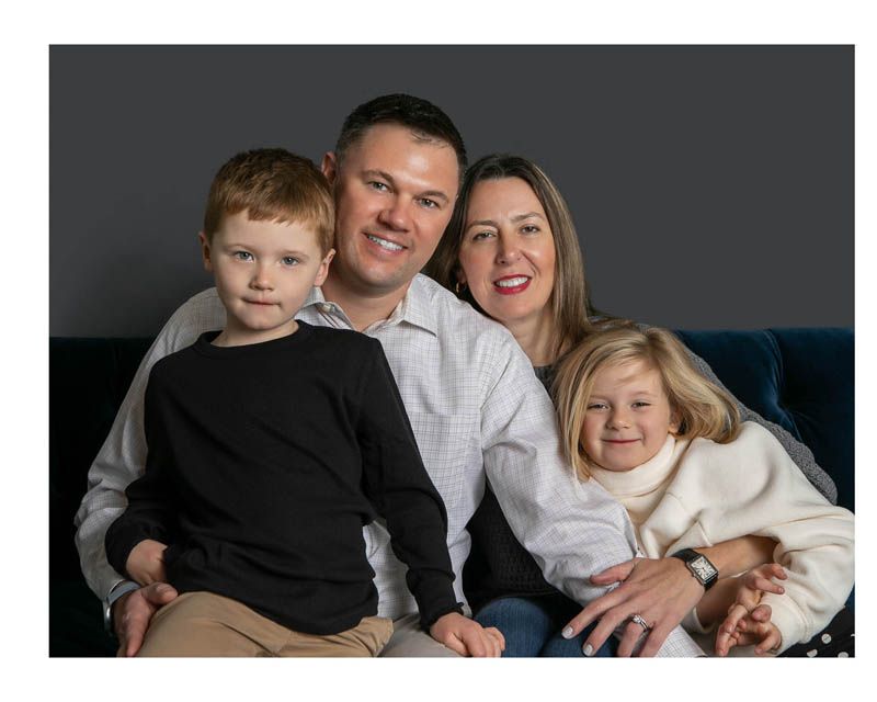 A loving family of four sitting together on a navy blue couch for a professional studio portrait.