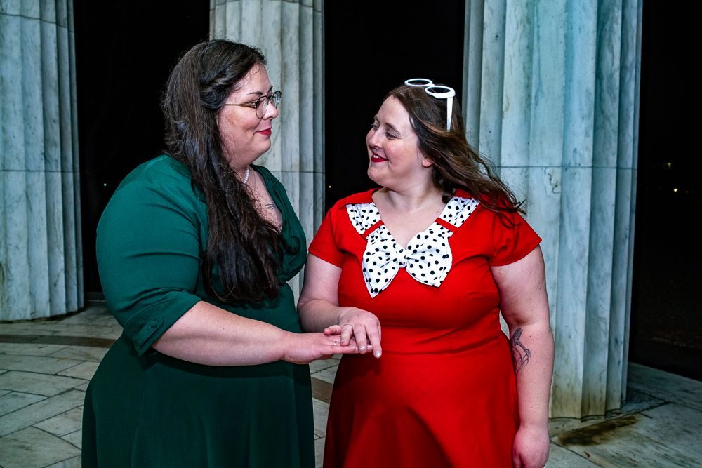 Two people in green and red outfits share a candid moment together in an outdoor setting.