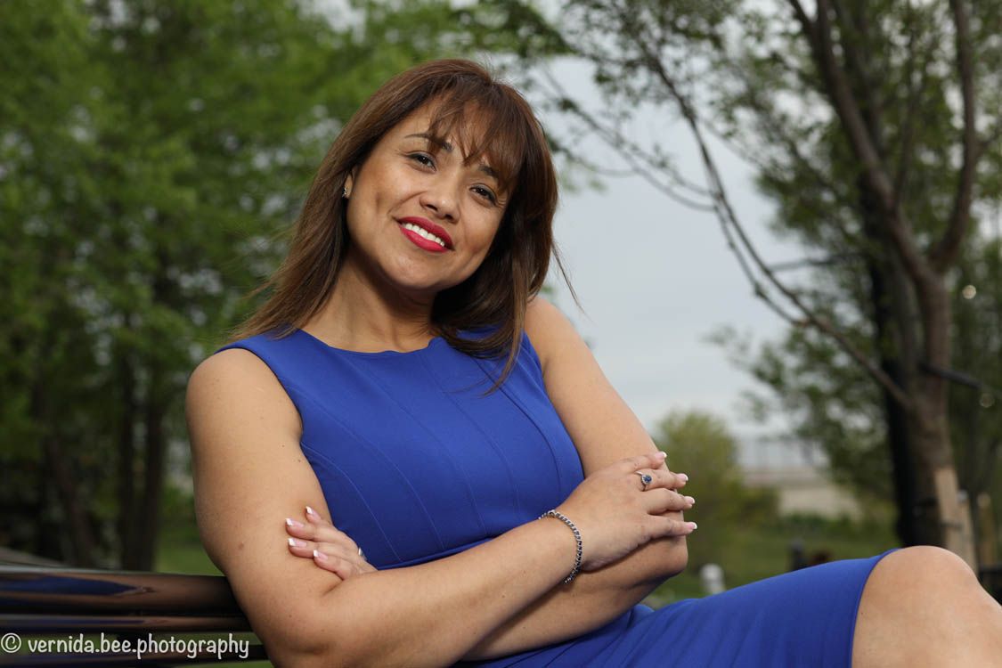 Woman in royal blue dress poses outdoors with bright smile and relaxed demeanor in natural setting.