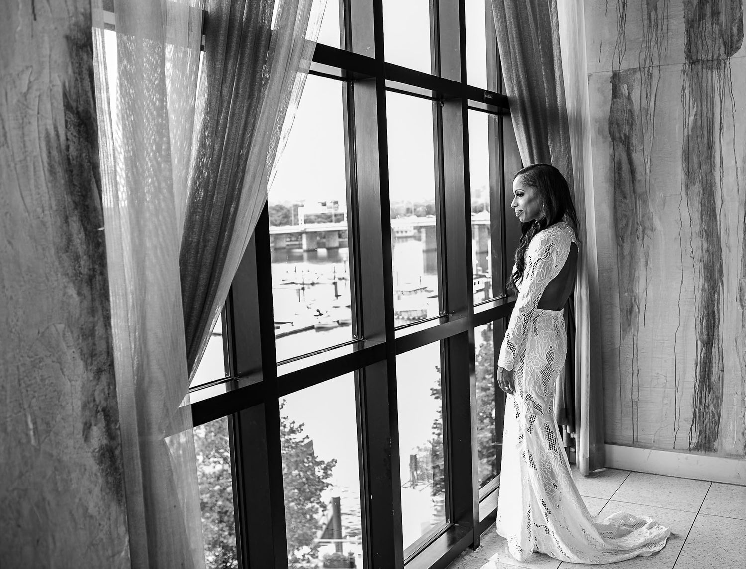 White flowy curtains frame a series of windows in an empty minimalist interior space.