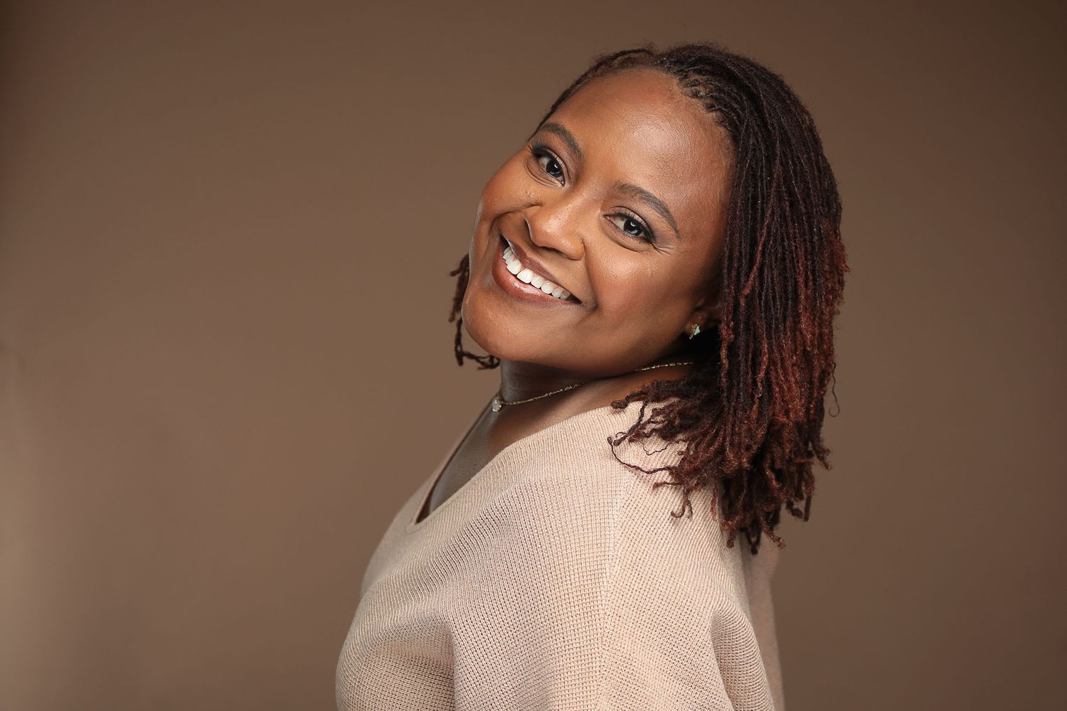 Natural light portrait series with cream sweater against warm brown background.