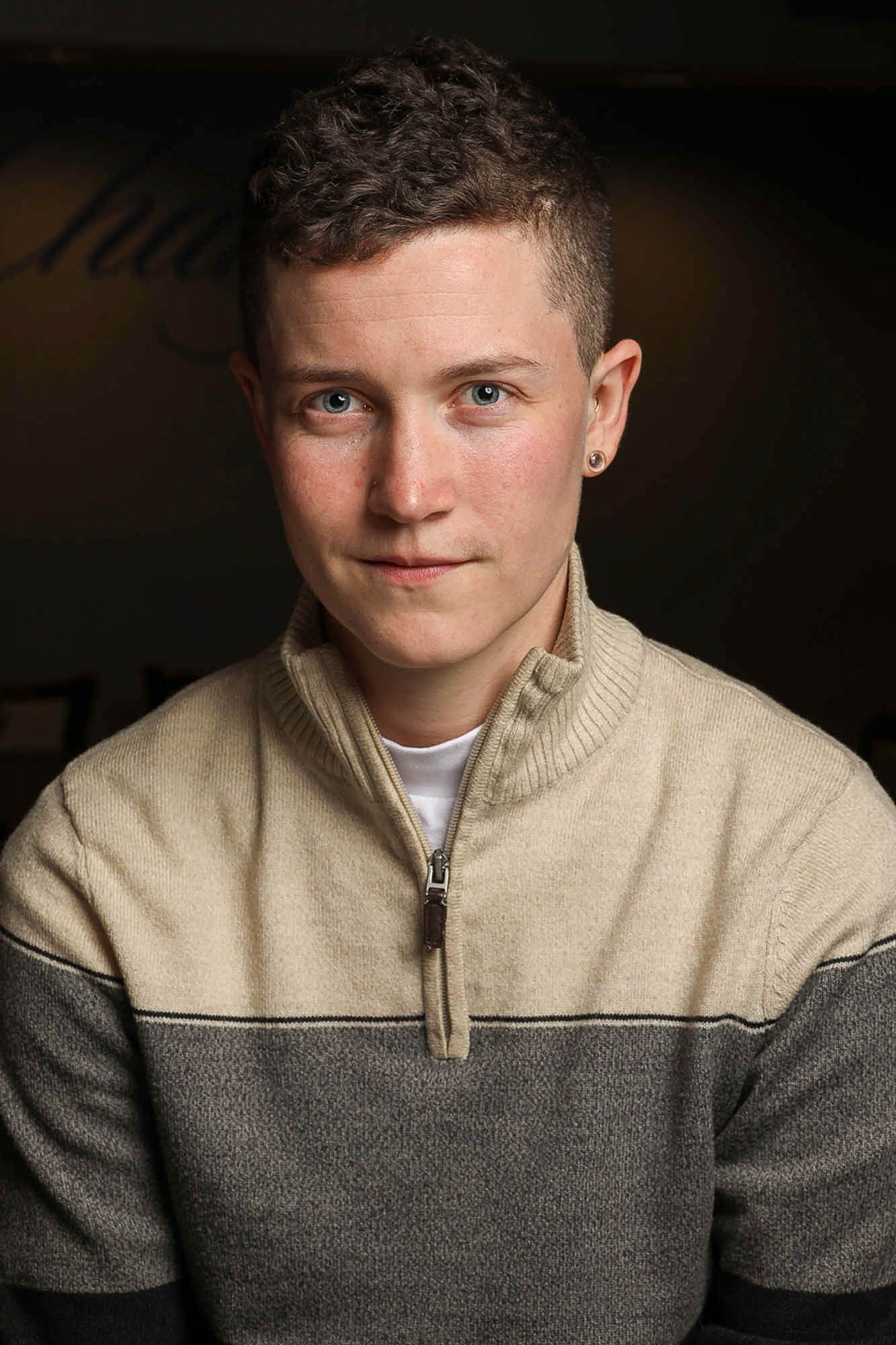 Portrait series of person in beige and grey colorblock knit sweater shown in multiple poses against dark background.