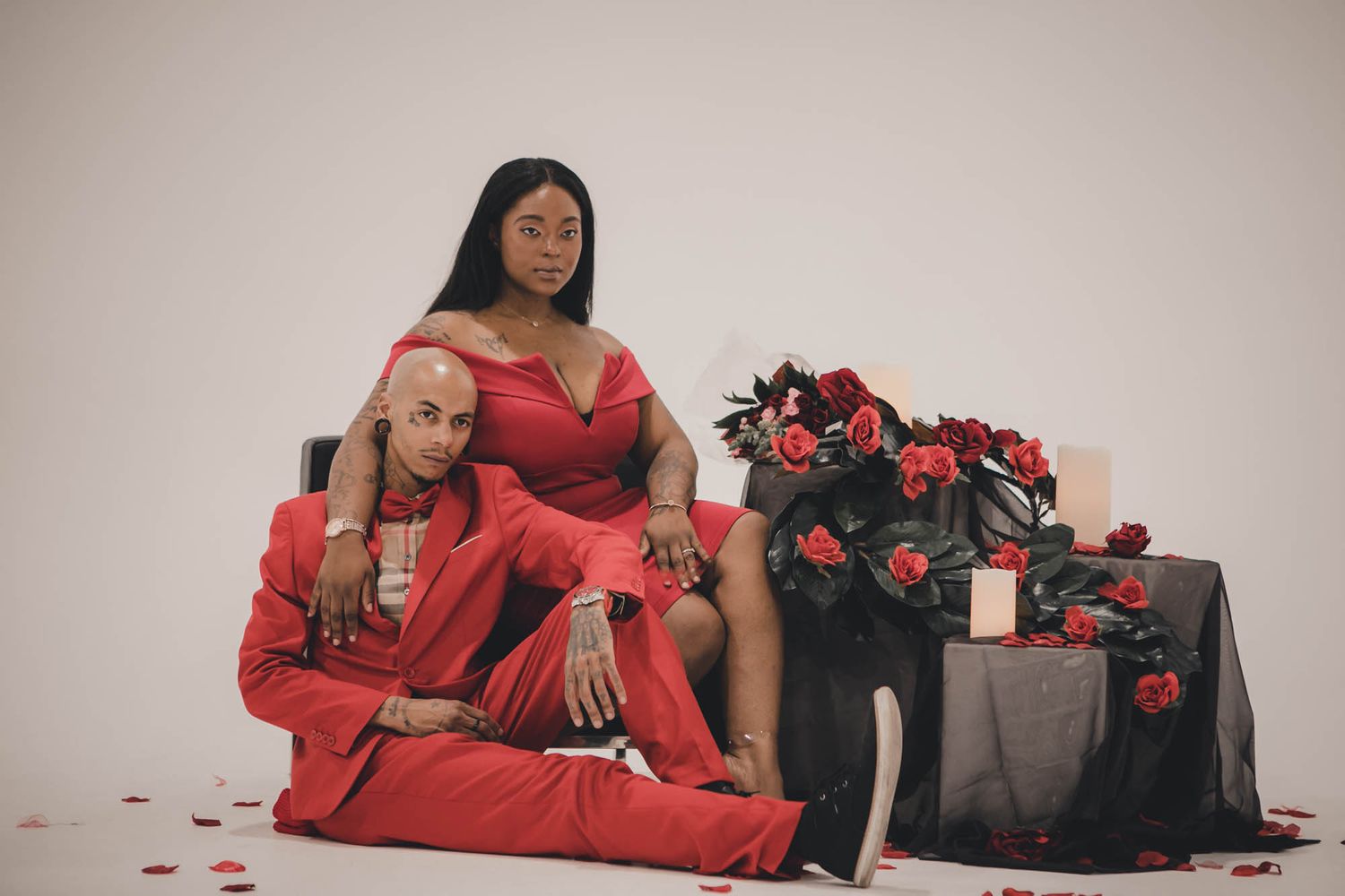 Elegant holiday photoshoot featuring red outfits and floral decor with rose petals scattered on the floor.
