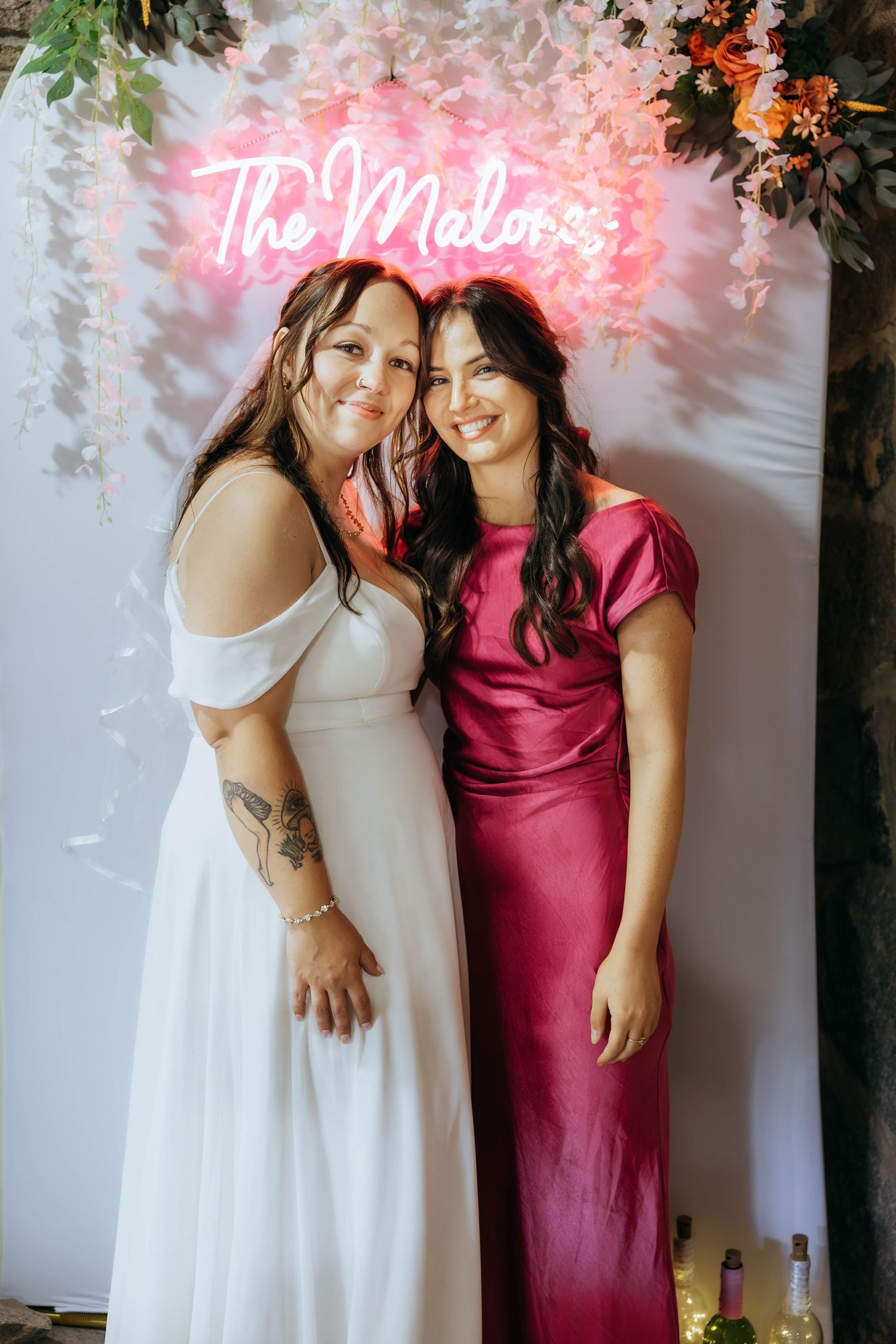 Wedding party members posing in white and burgundy dresses against floral backdrop.