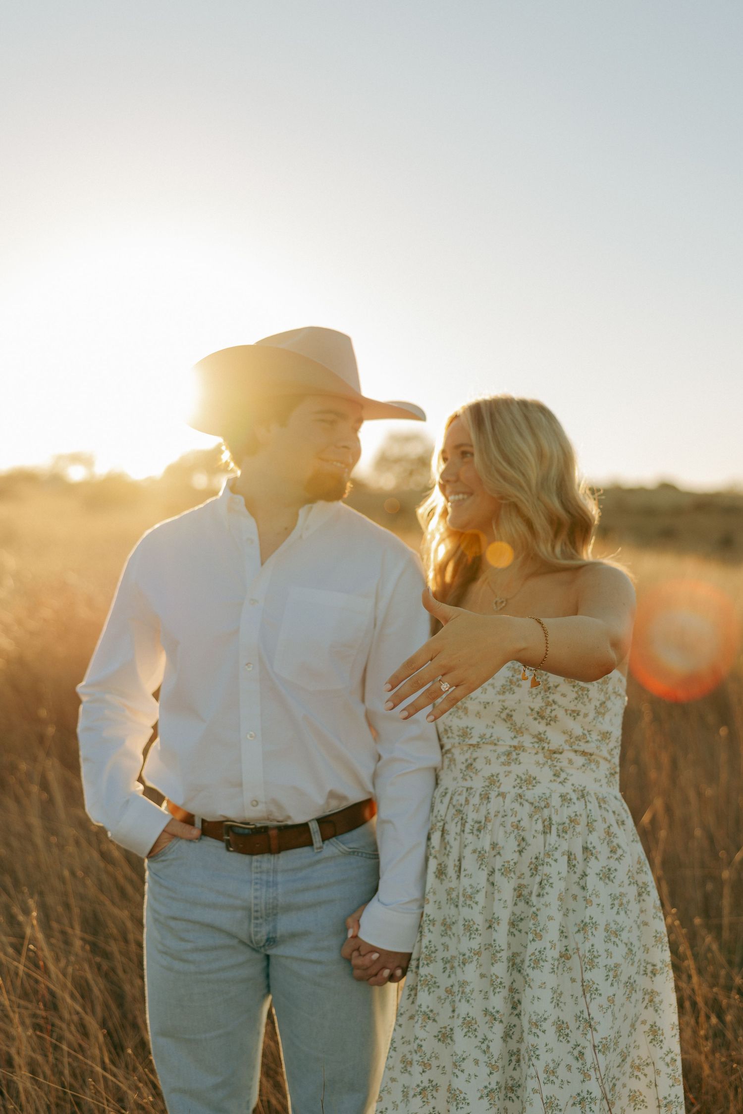 A newly engaged couple sharing tender moments in a golden field at sunset.