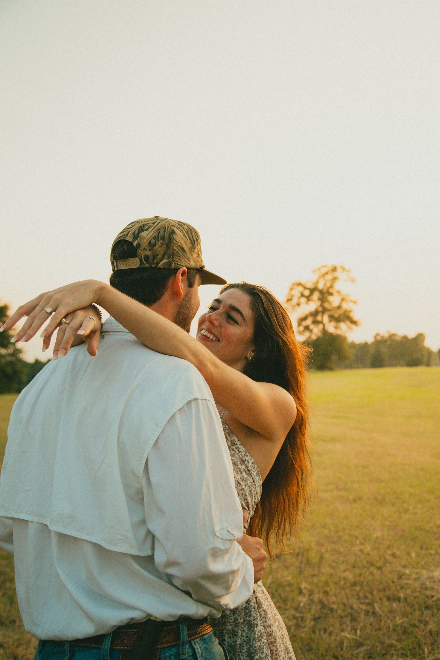 Romantic couple embracing in a sunny field during a golden hour engagement photoshoot.