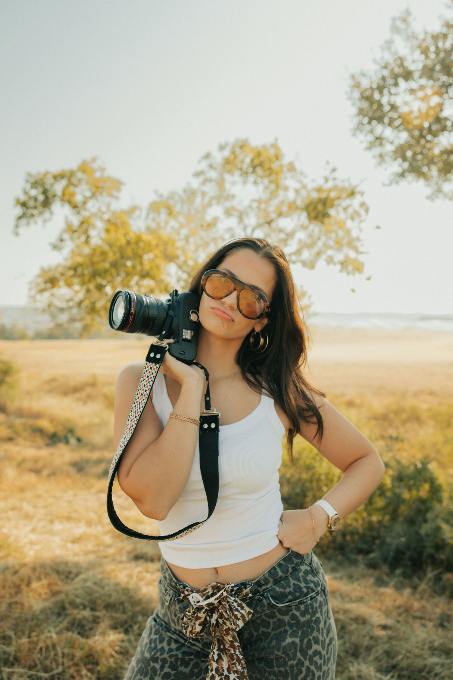 Photographer with camera and sunglasses poses against golden field backdrop.