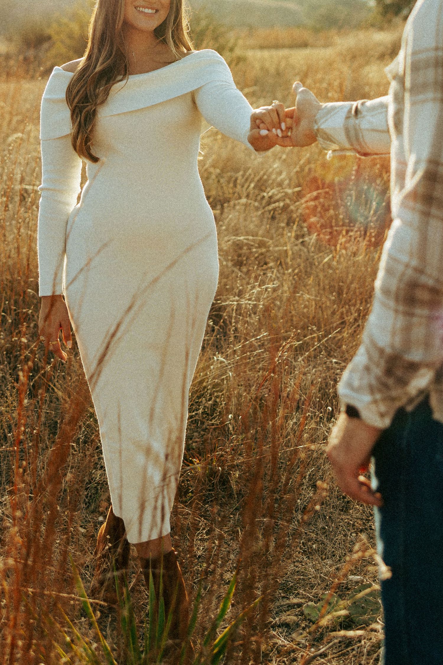 A couple embraces in a golden sunlit field during sunset in maternity photoshoot.