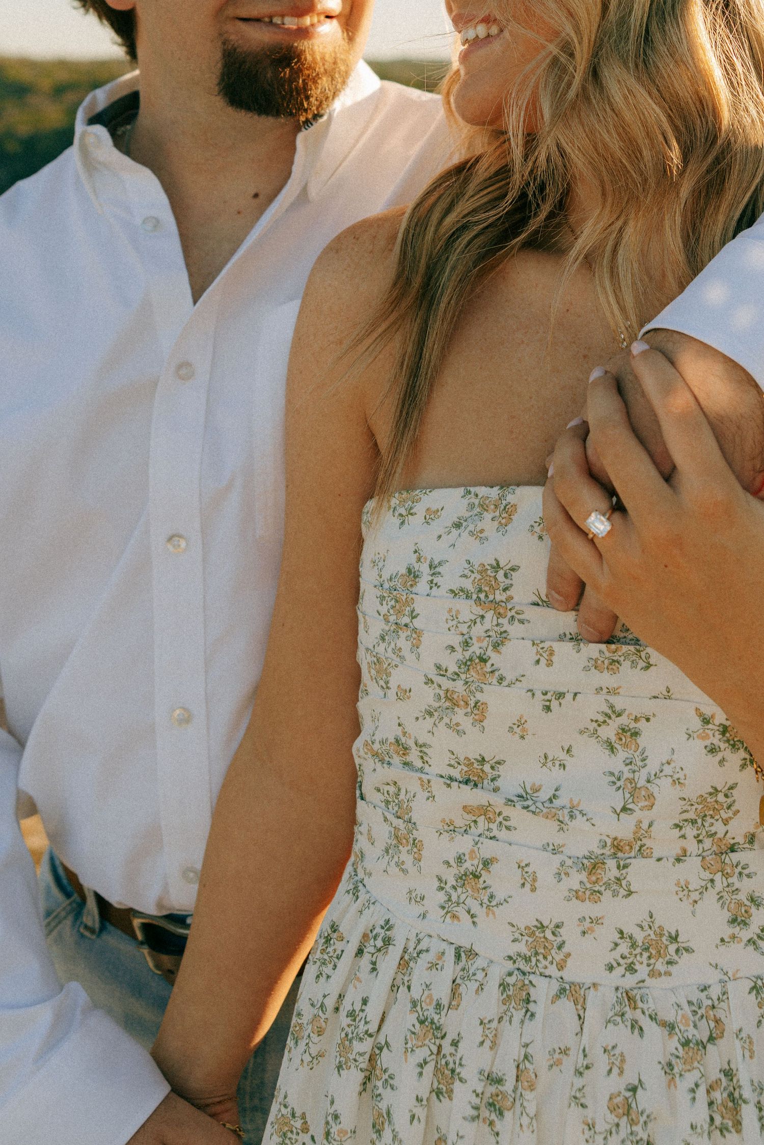Close-up shot of a newly engaged couple in white and floral dress sharing an intimate moment in golden sunlight.