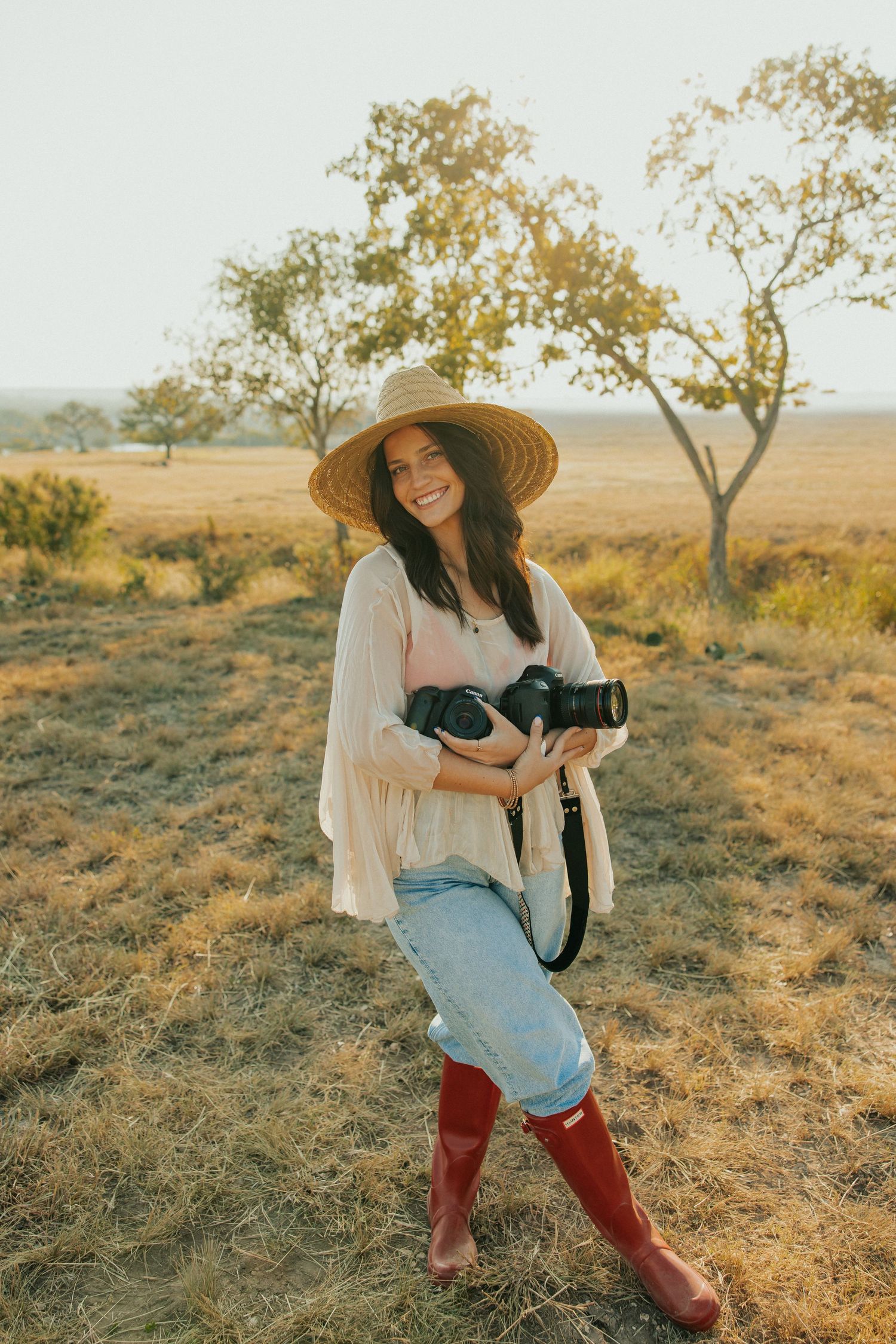Photographer in straw hat and red boots captures images in sun-drenched countryside.