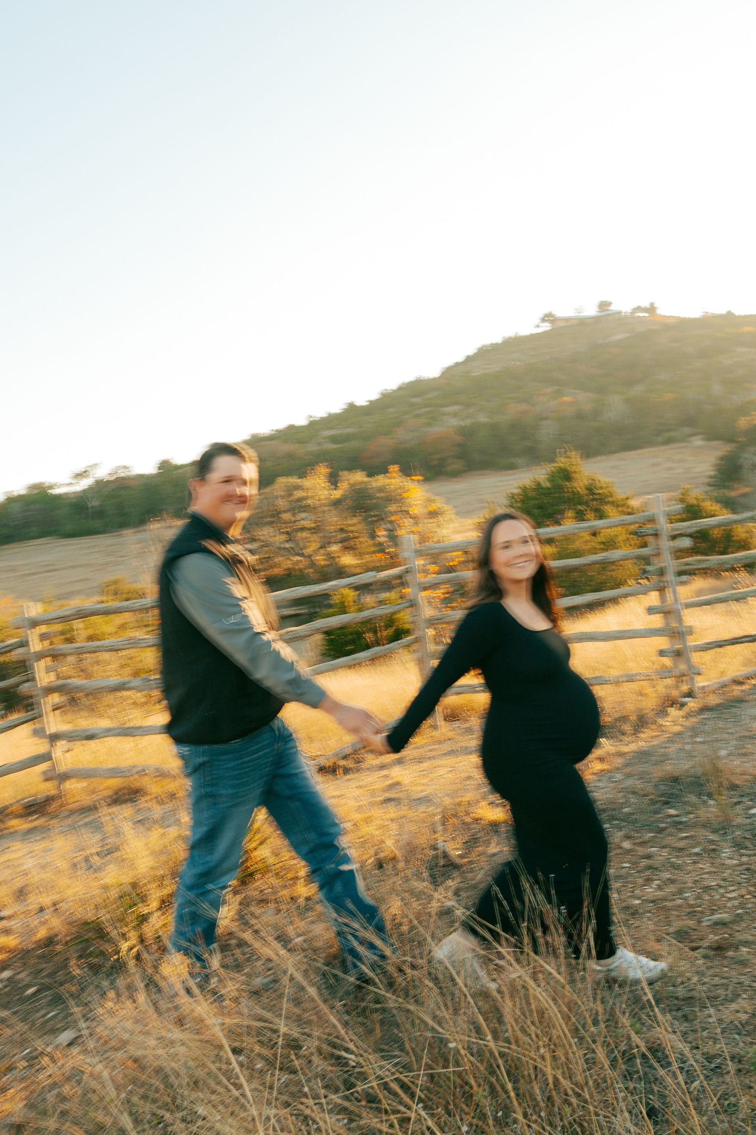 Couple dancing and twirling in a golden field at sunset during maternity photoshoot.