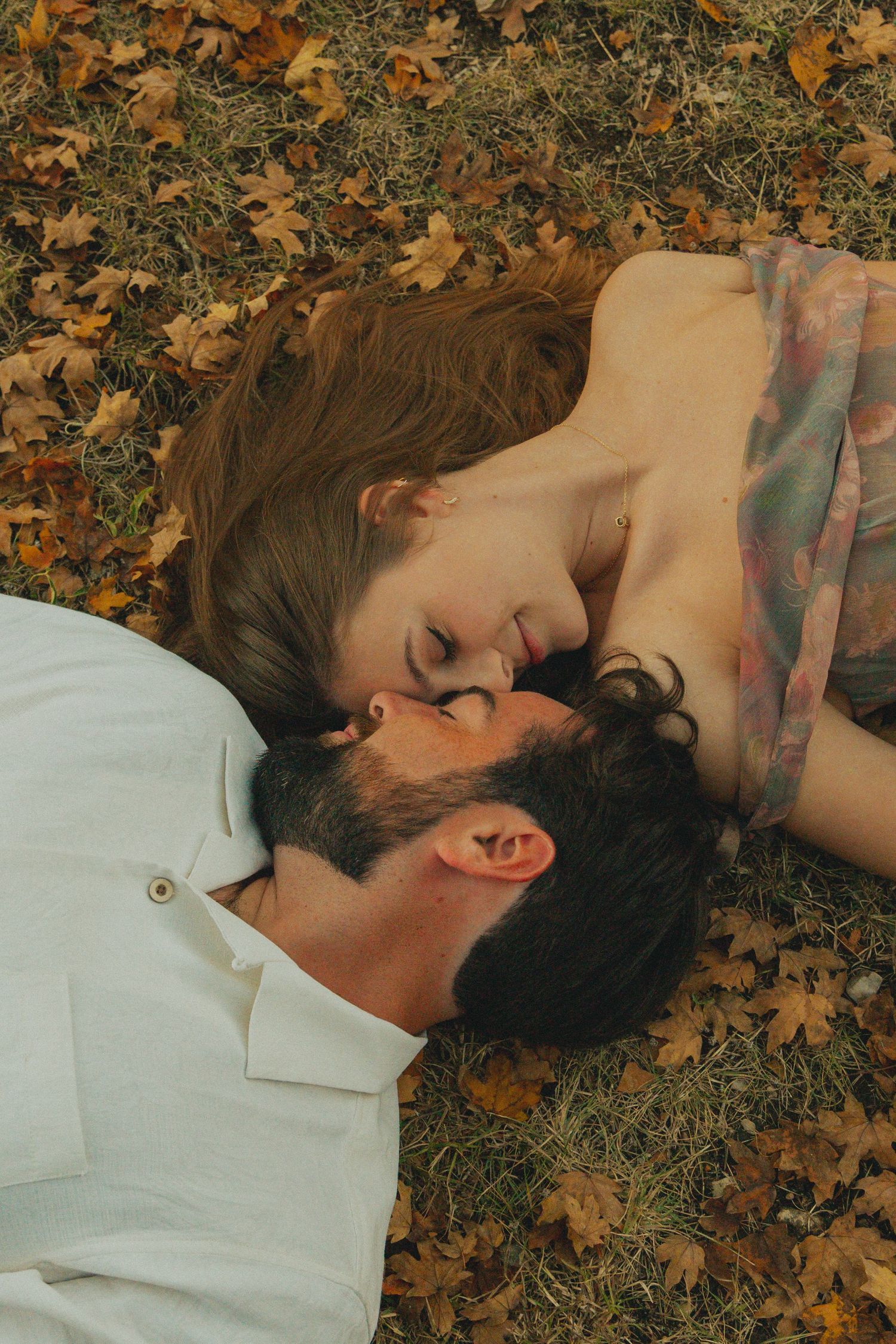 A couple lying in autumn leaves sharing an intimate moment together.