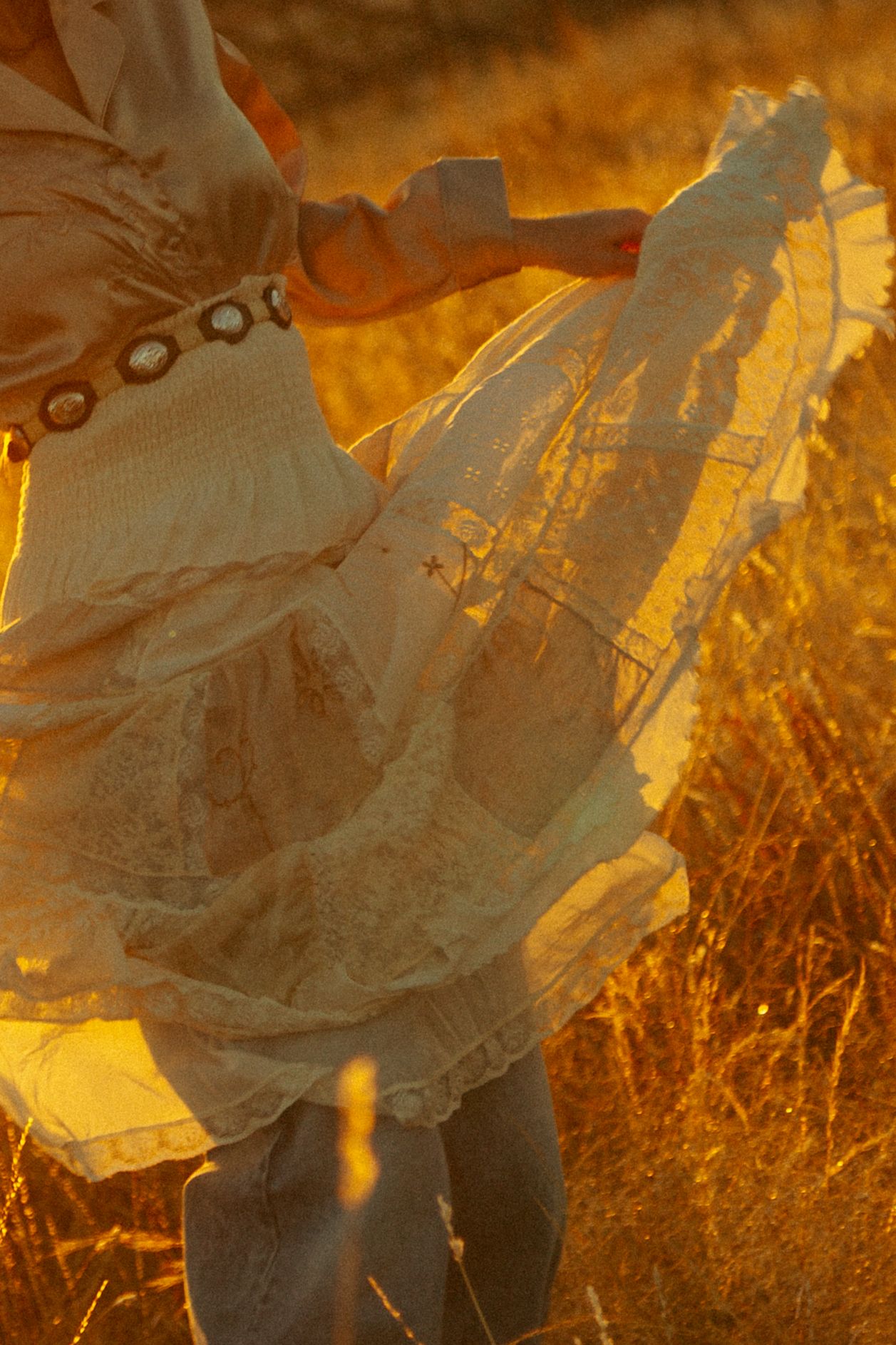 Silhouette of flowing lace fabric against golden sunset light in a field.
