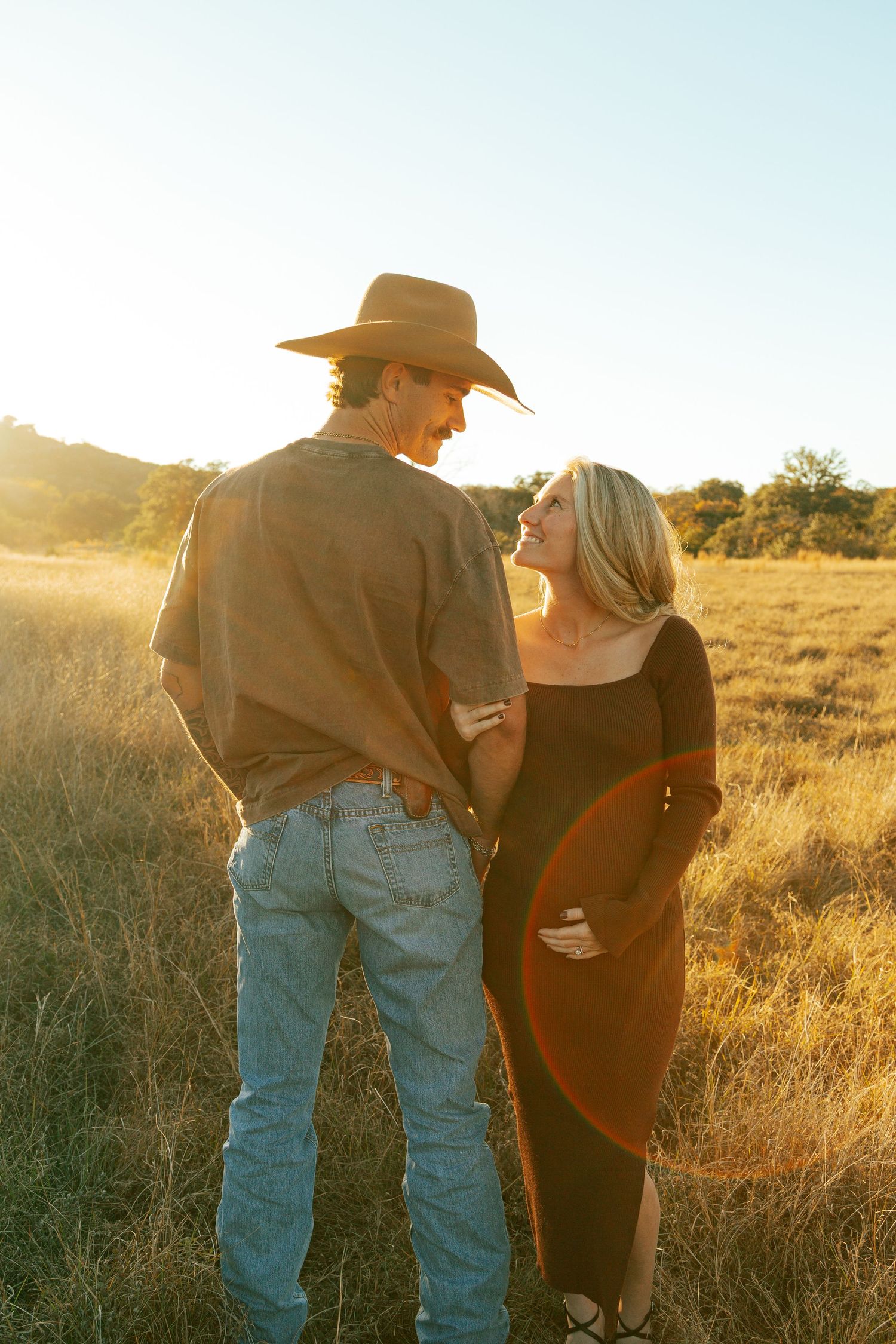 A couple embraces in a sun-drenched field during golden hour.