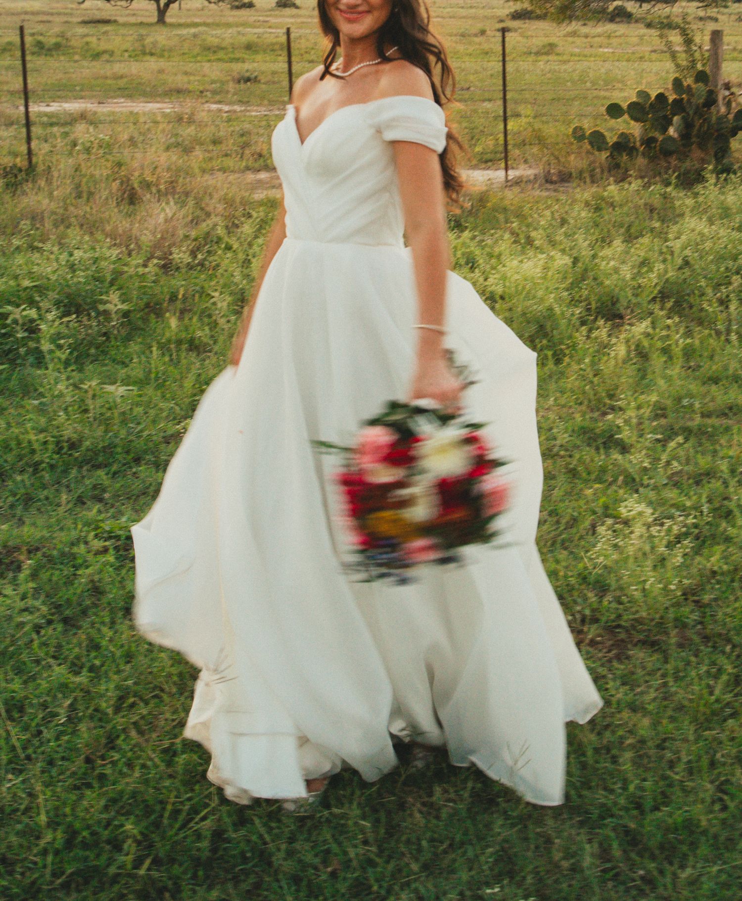 White wedding dress flowing in the breeze as bride walks through a green field.