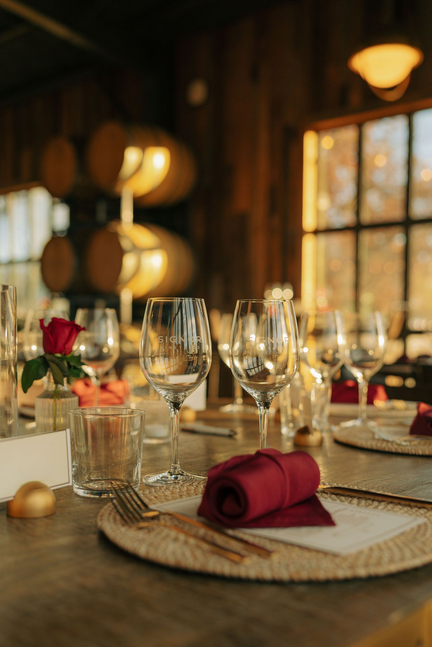 Elegant table settings with burgundy napkins and wine glasses in warm lighting.