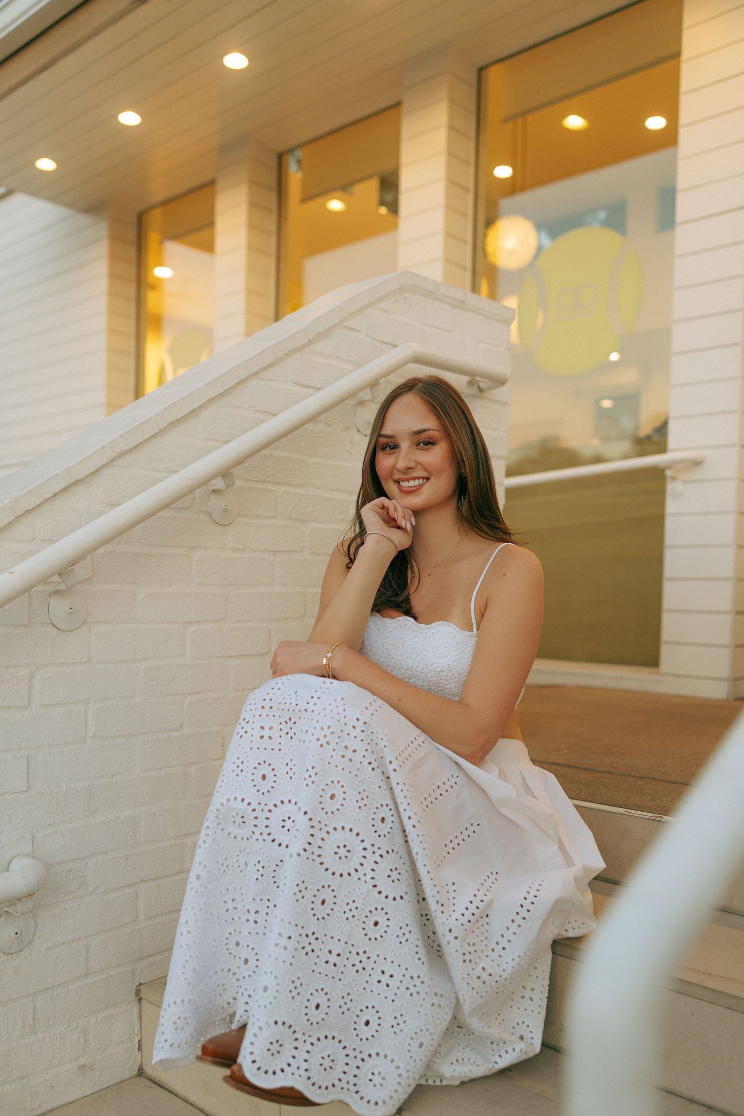 A woman in a white dress creates an elegant scene on white painted brick steps with warm interior lighting.