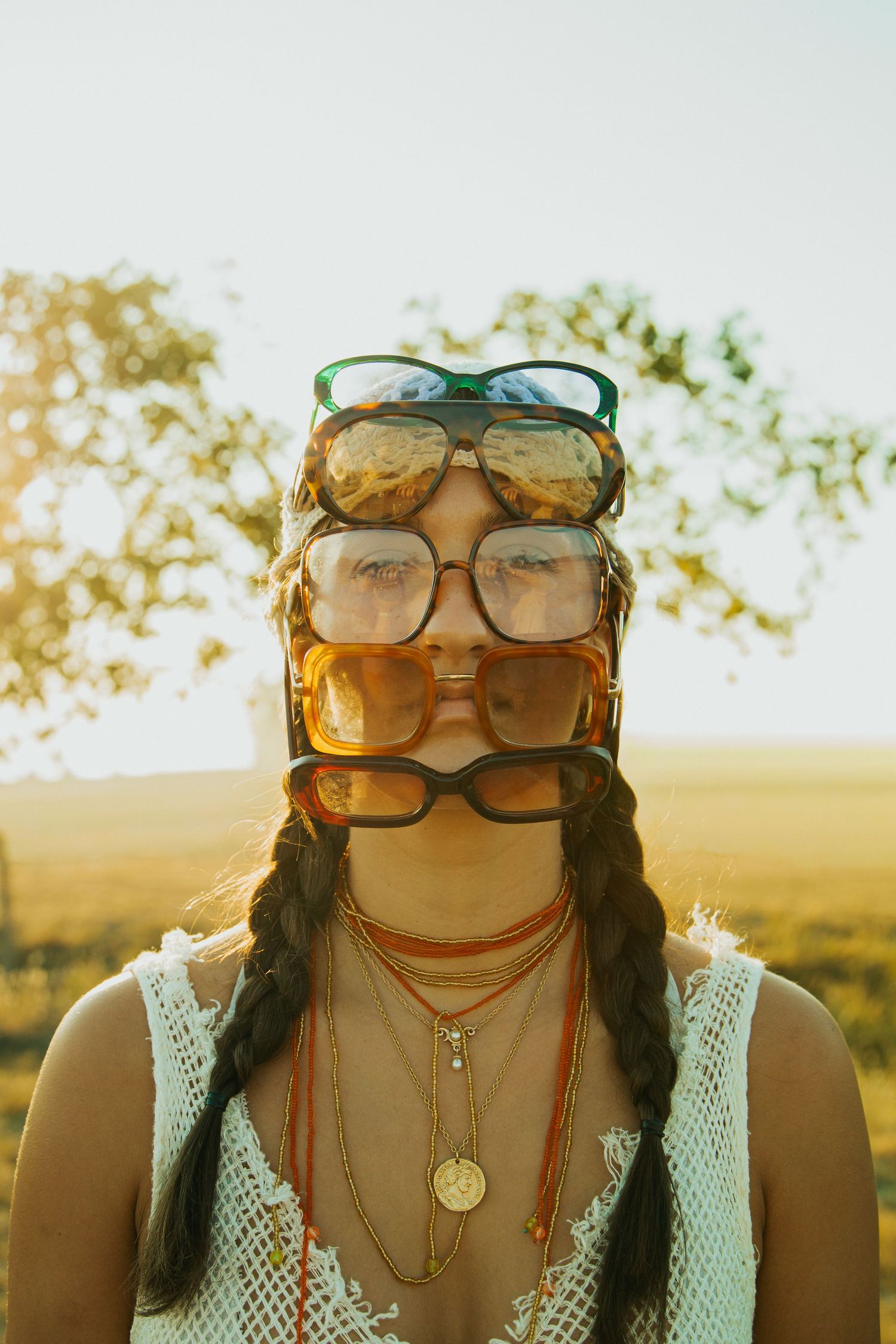 Artistic sunlit portrait showing a woman wearing various pairs of glasses reflecting golden light at sunset.