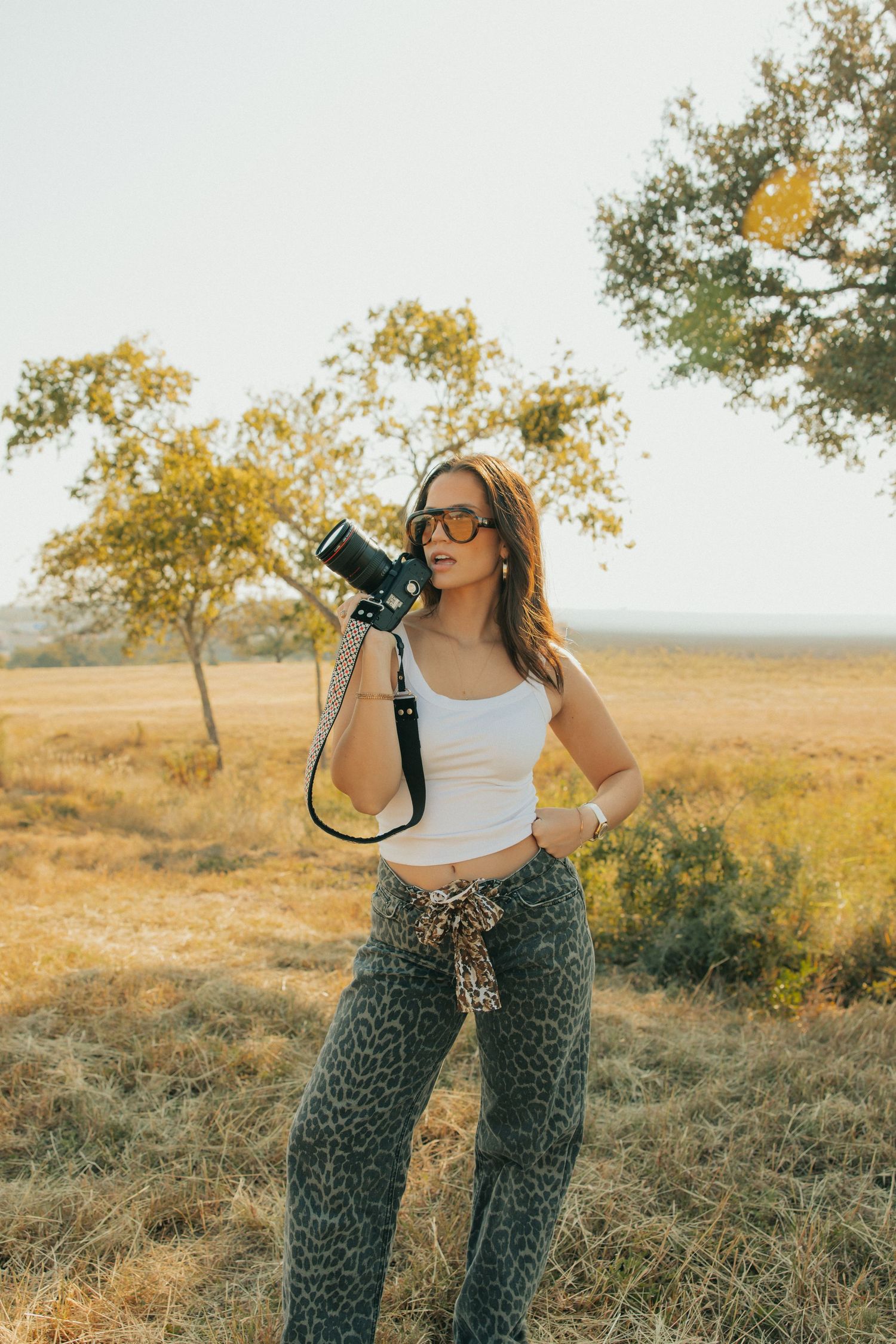 Photographer with camera poses in during golden hour countryside shoot.