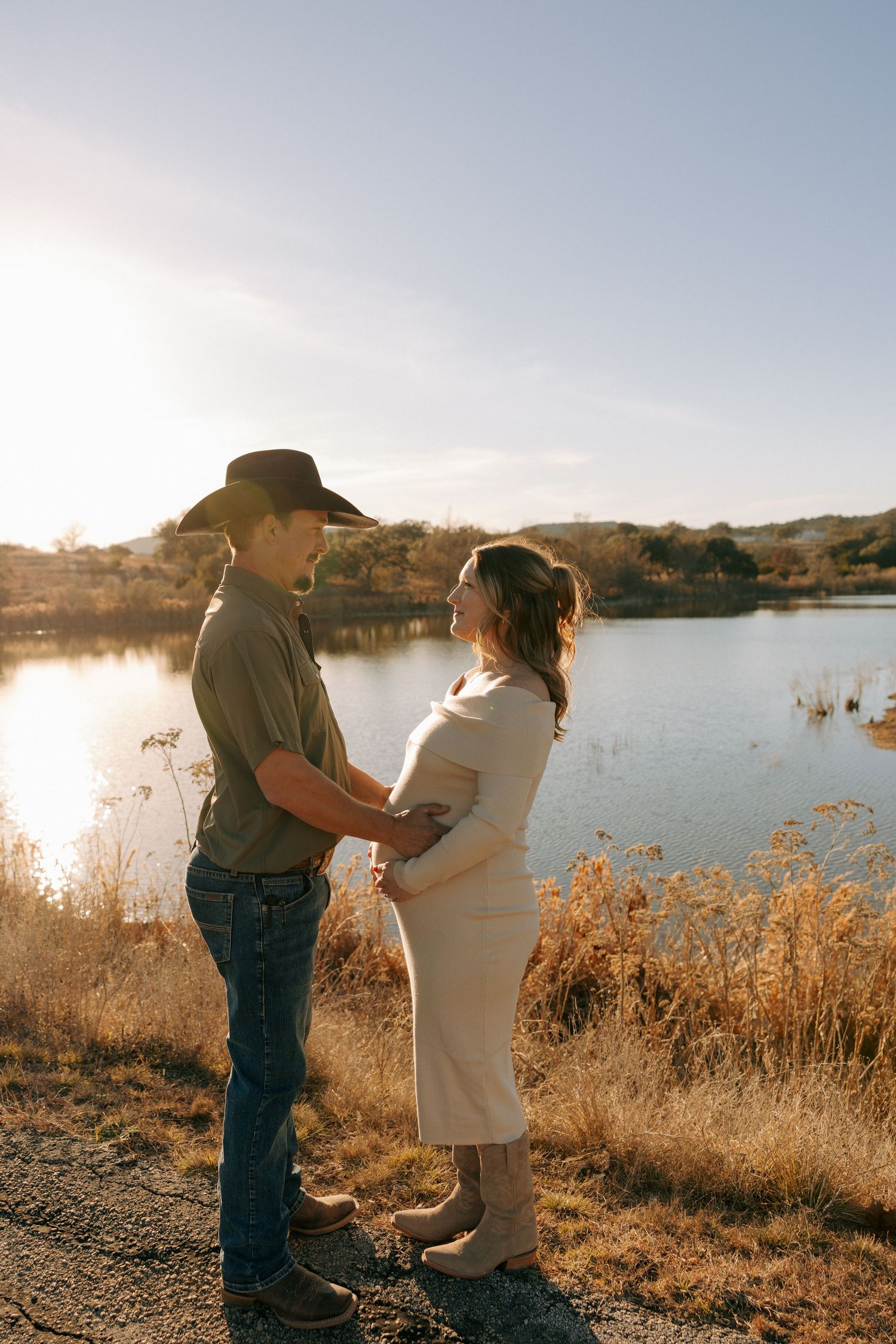 Couple standing by a lake during golden hour with mountains in the background.