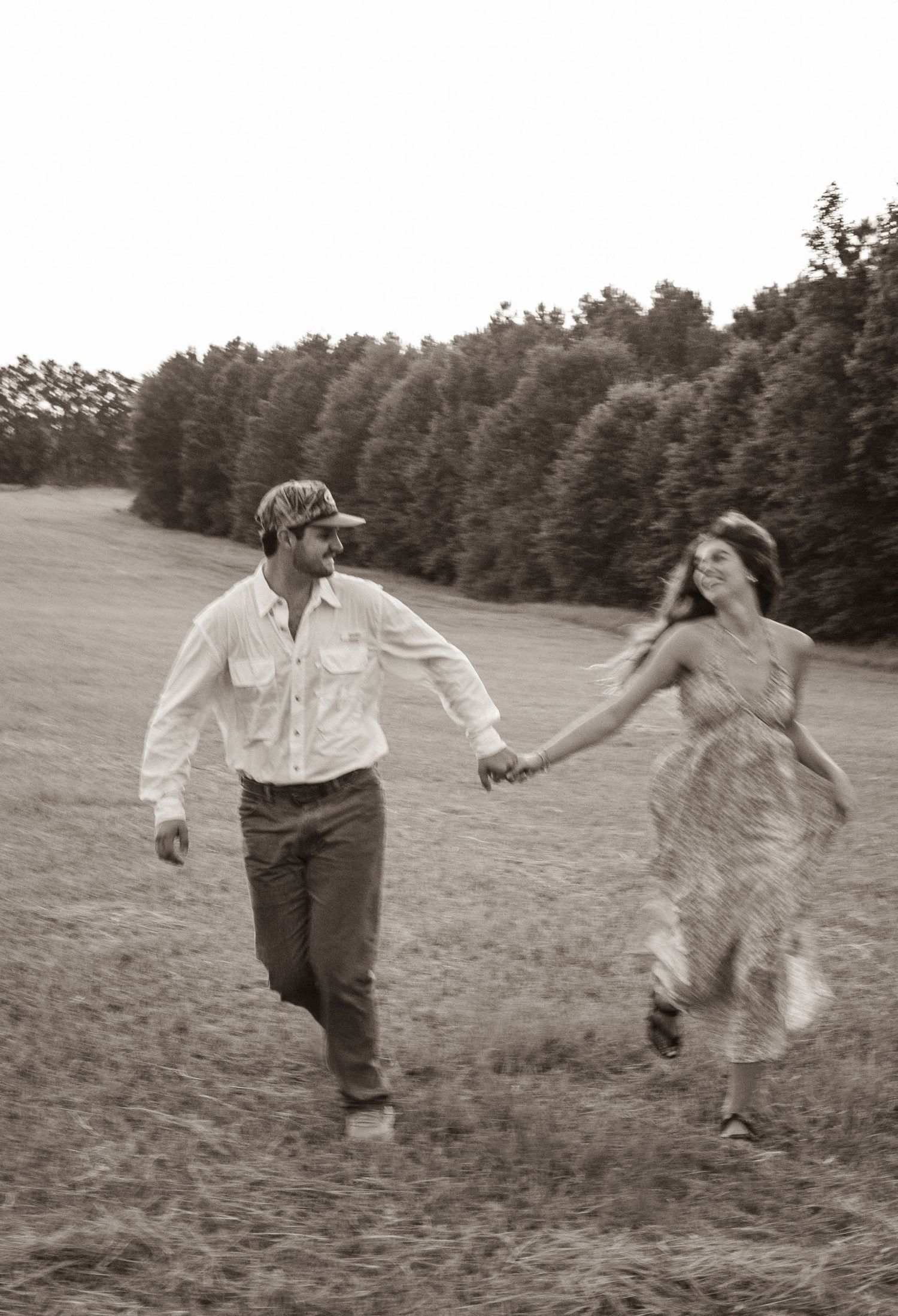 Black and white image of a couple running through a meadow holding hands.
