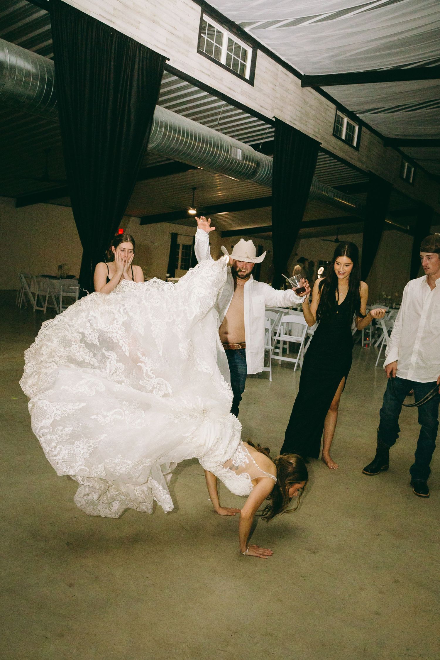 Bride in wedding dress performs dance move at reception.
