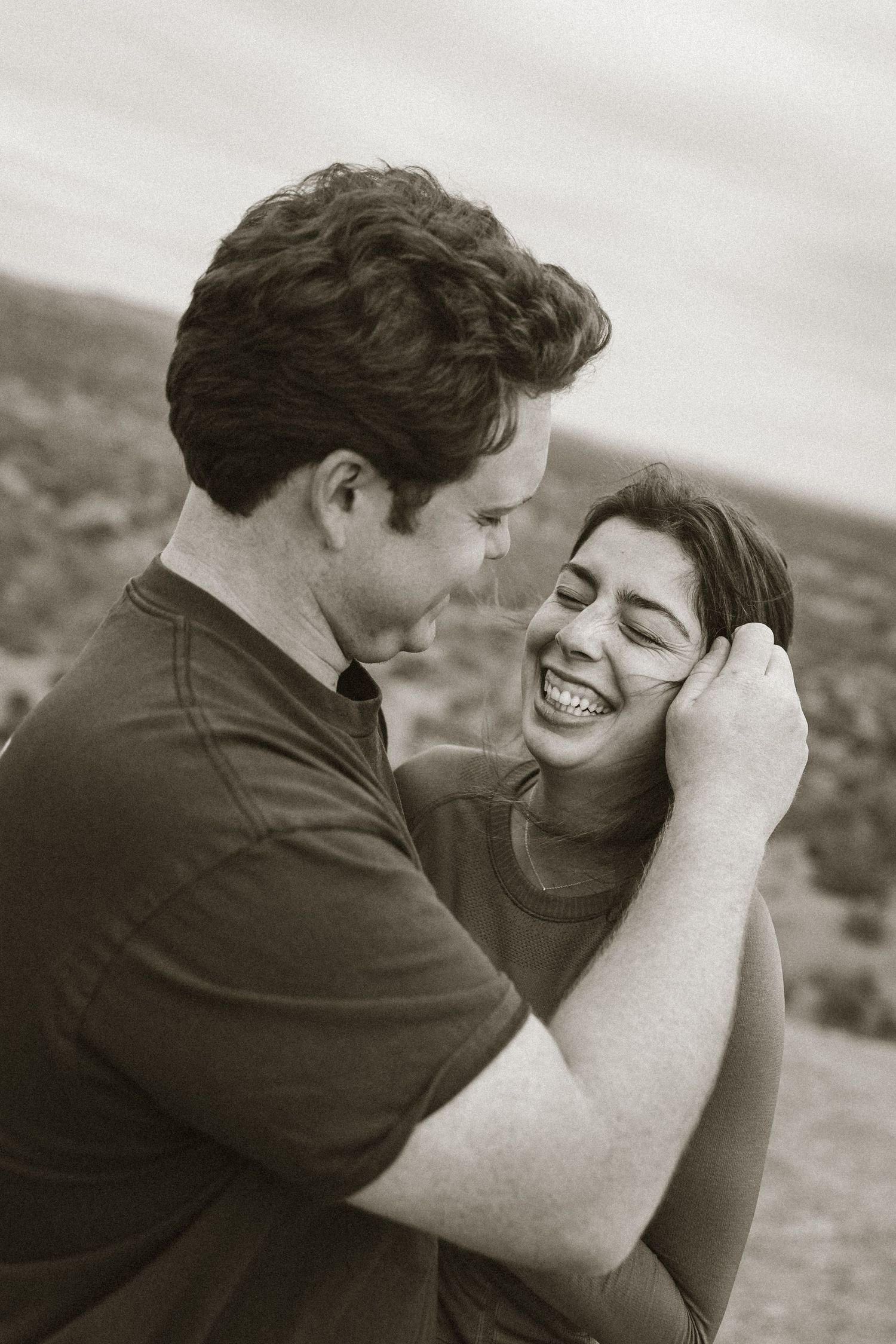 Black and white portrait of couple sharing a tender moment on a hilltop.