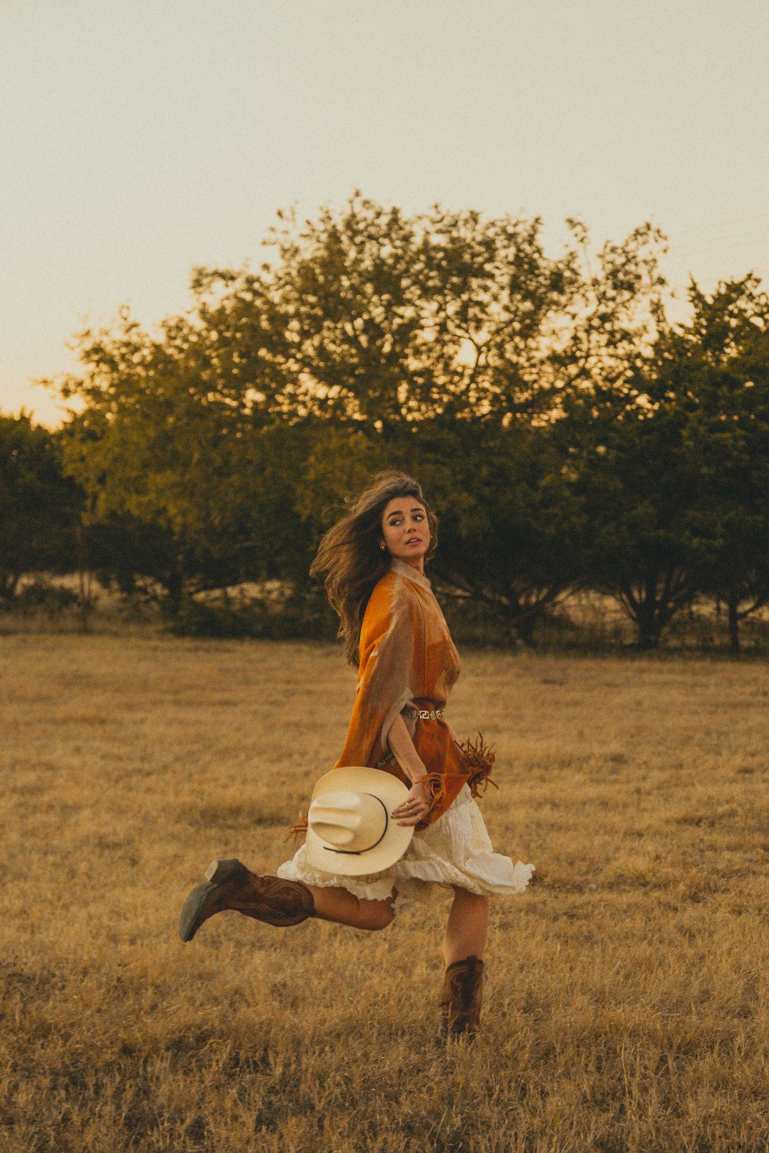 Playful poses in a rustic field wearing western-inspired outfit with fringe detail.
