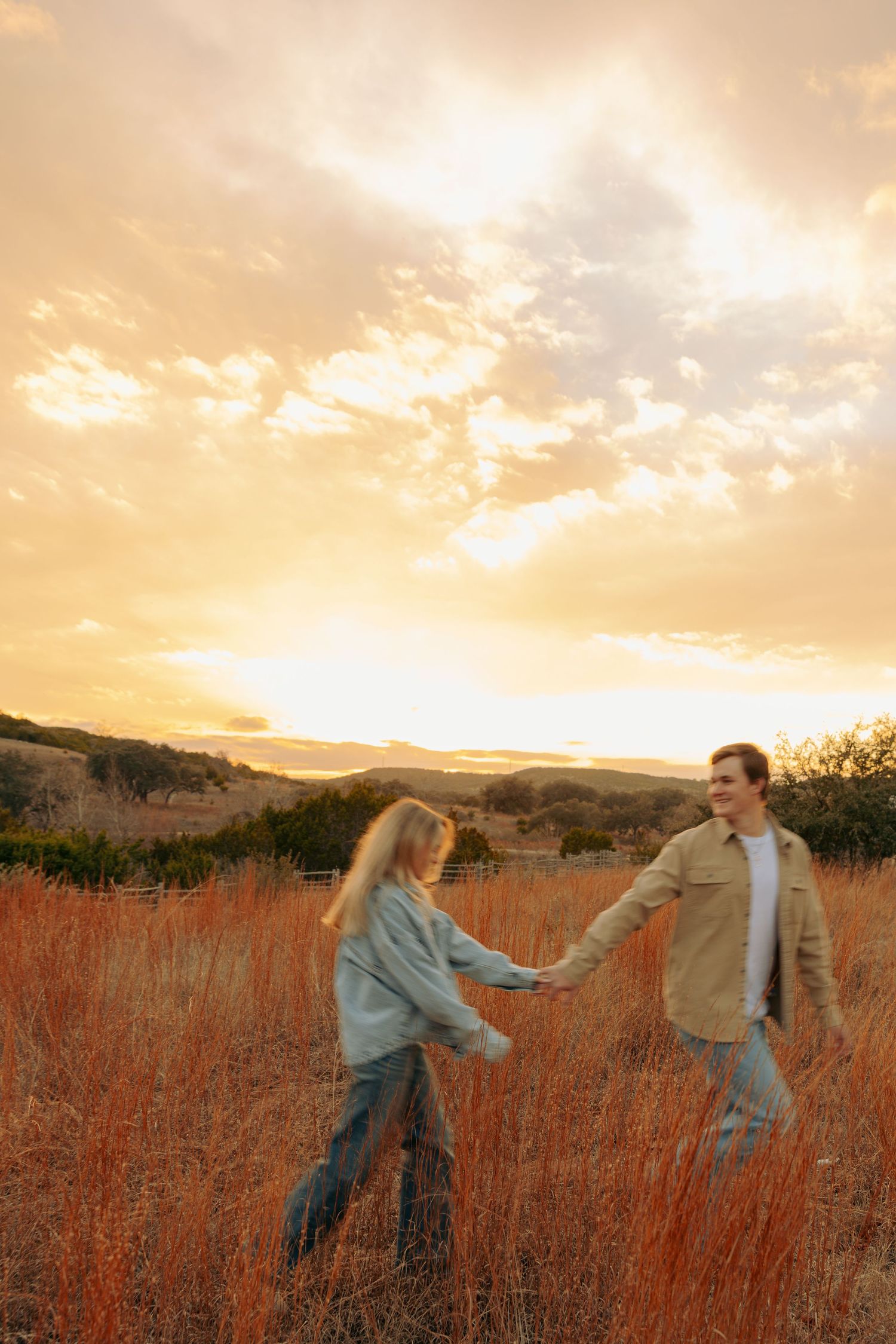 Couple dancing through tall grass during a golden sunset in the countryside.