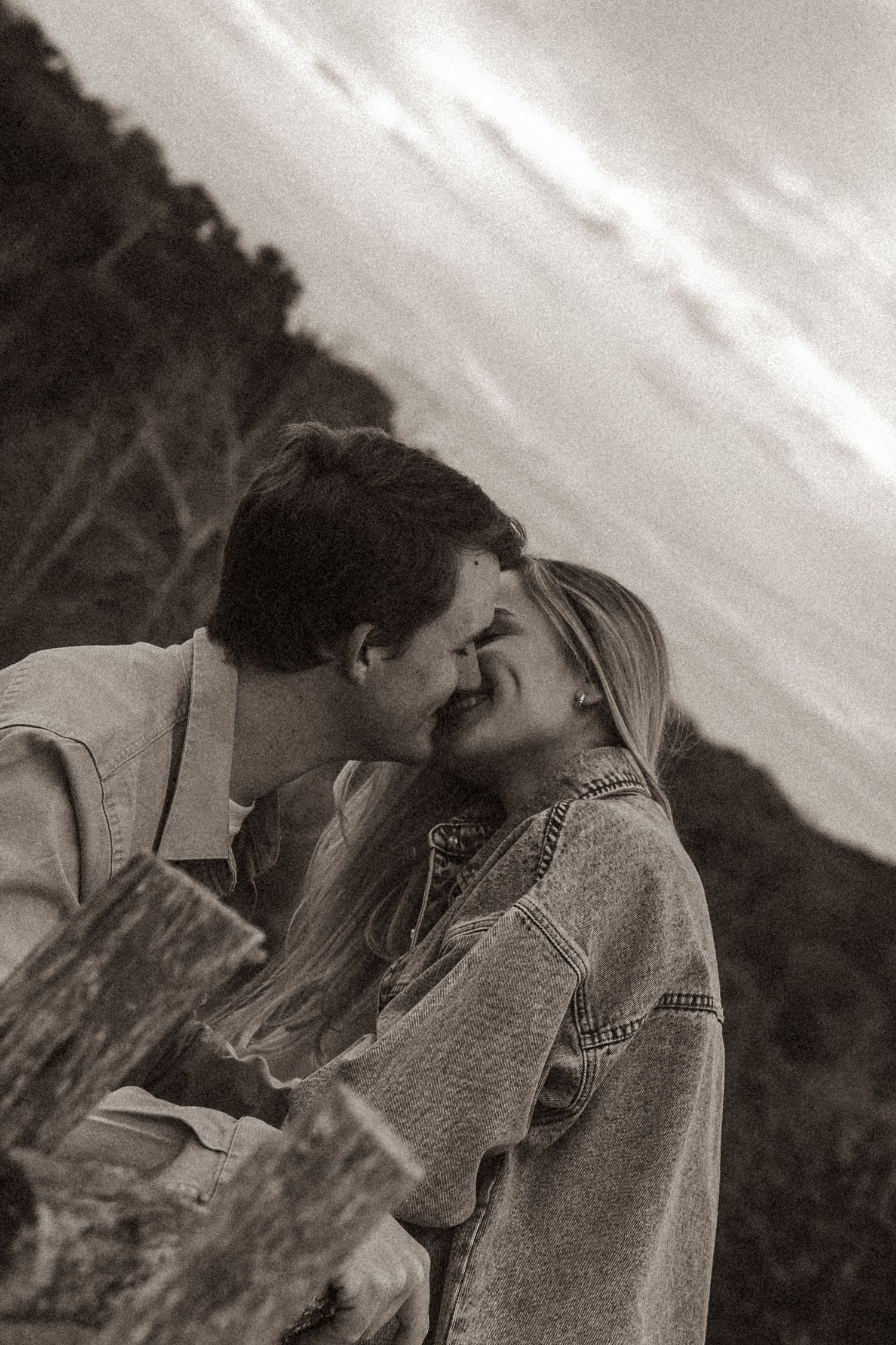A tender black and white moment captured between a couple against a cloudy sky.