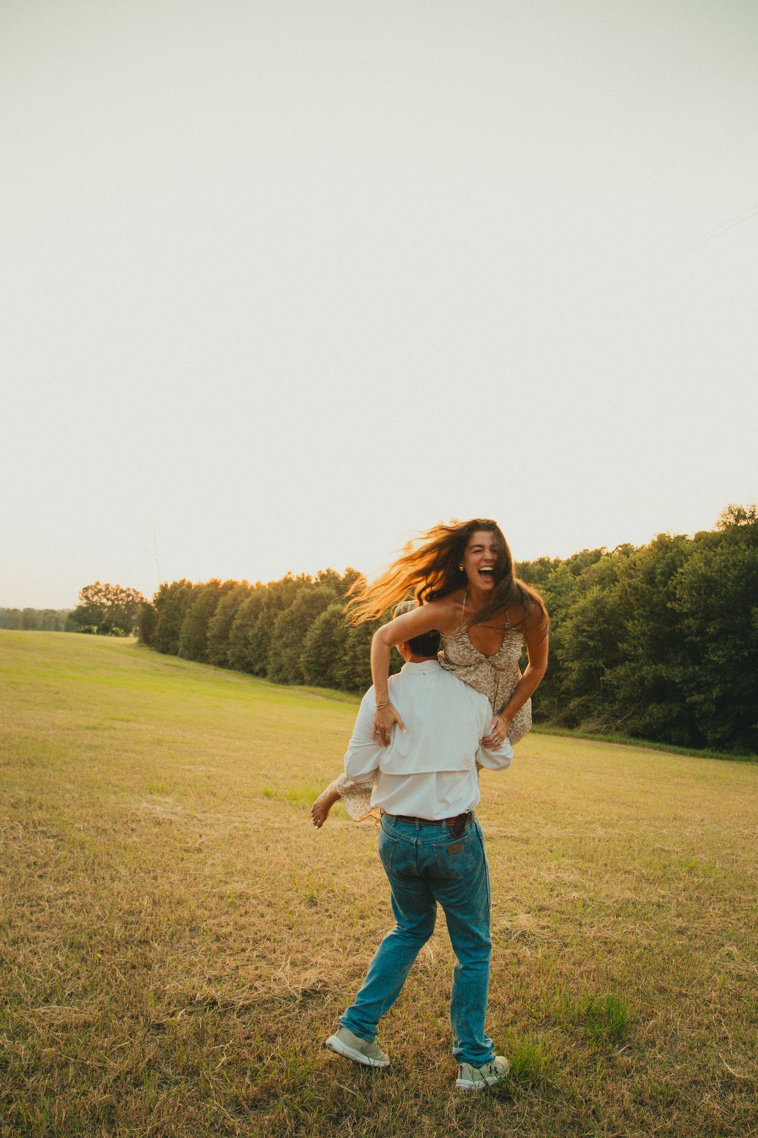 Couple dances and laughs together in a sunlit meadow during golden hour.