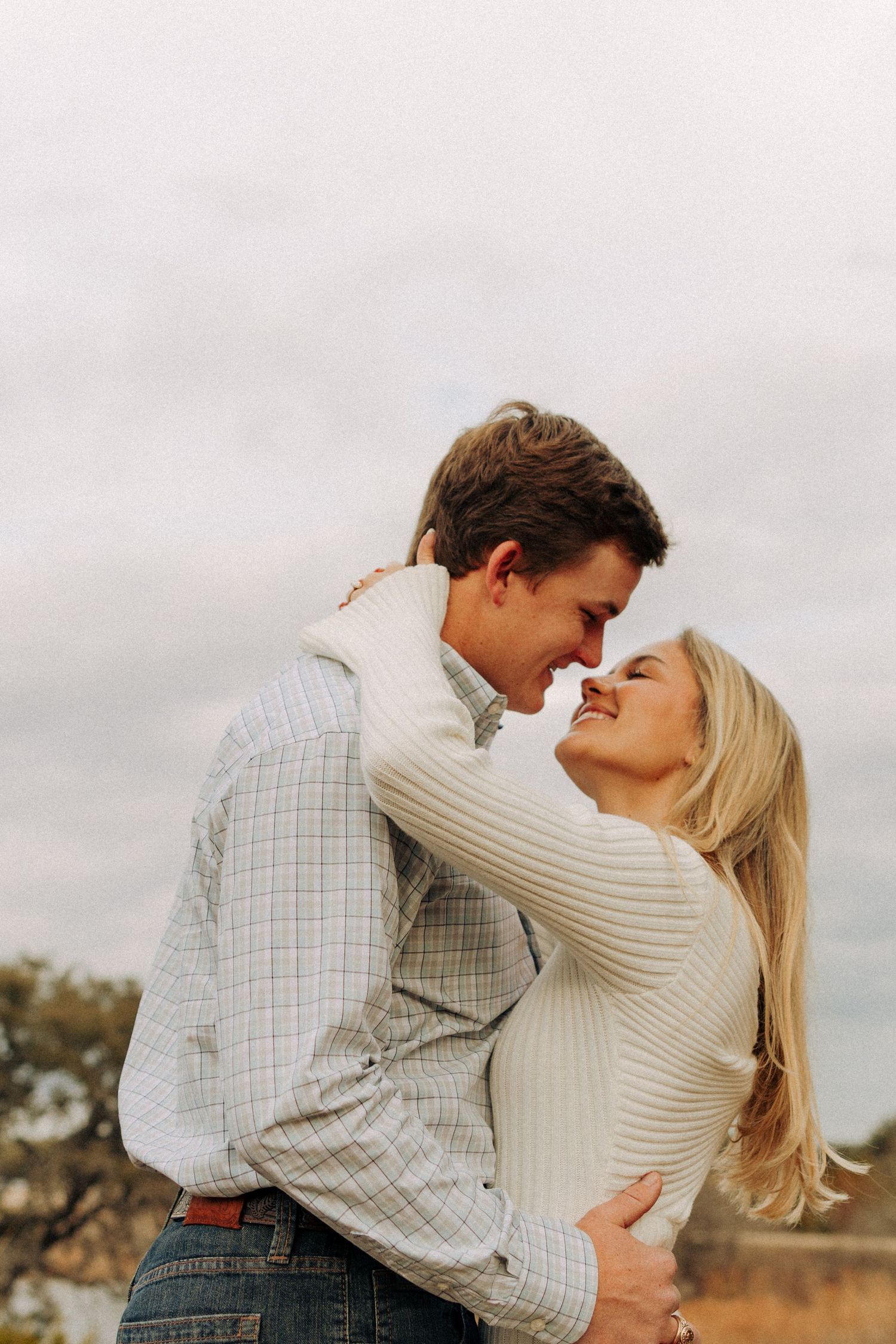 Romantic couple embraces in a tender moment against a cloudy outdoor backdrop.
