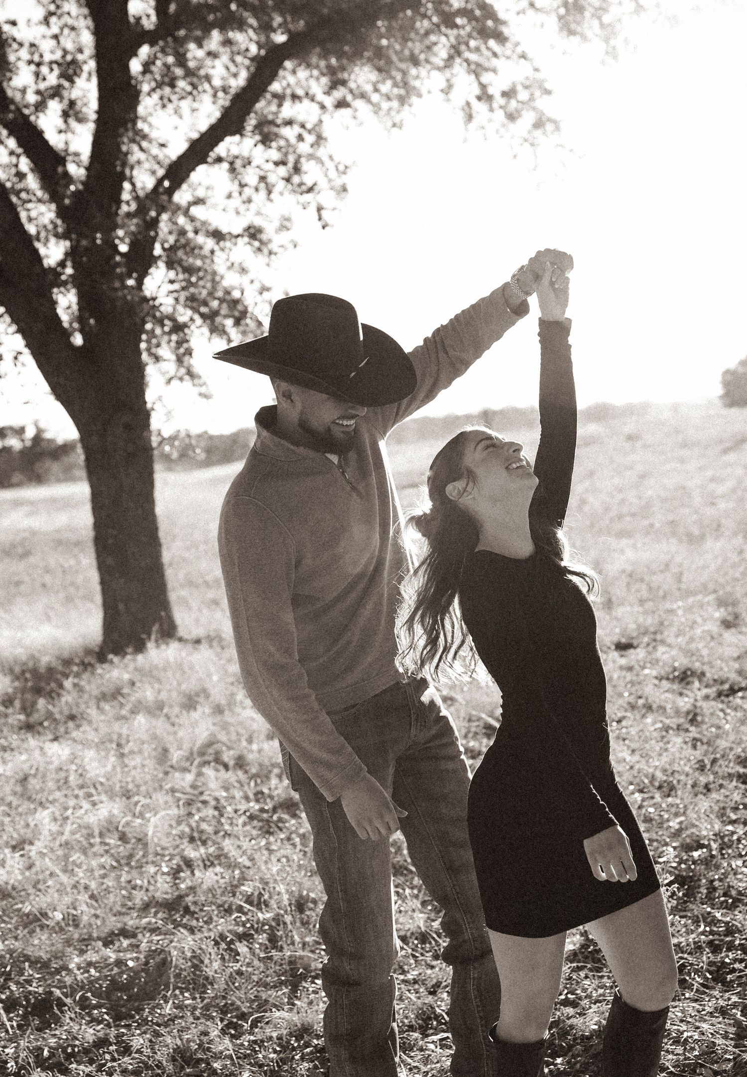 Dancing couple silhouetted against sunlit trees in a field.