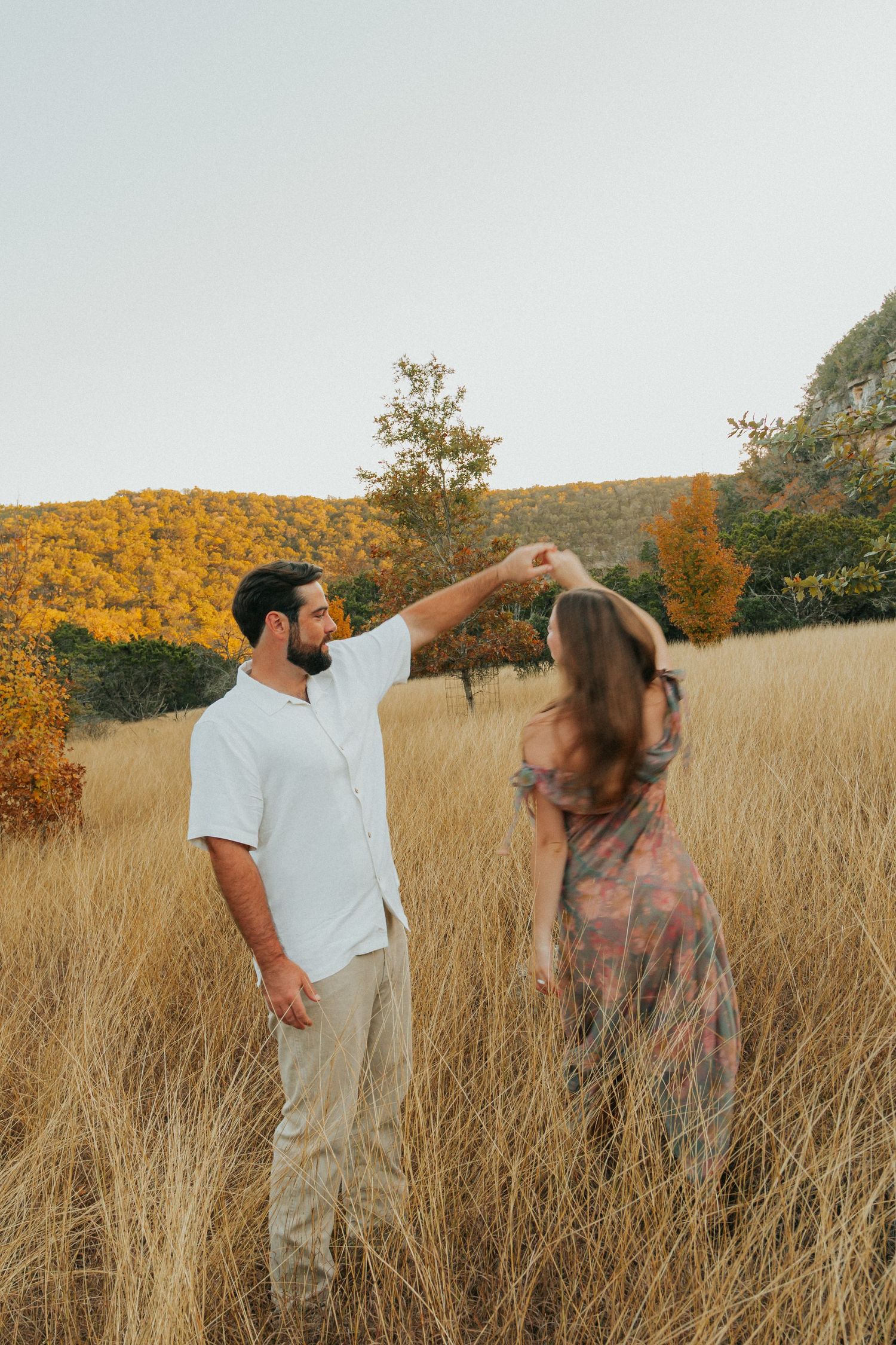 Couple dancing playfully in tall golden grass during sunset.