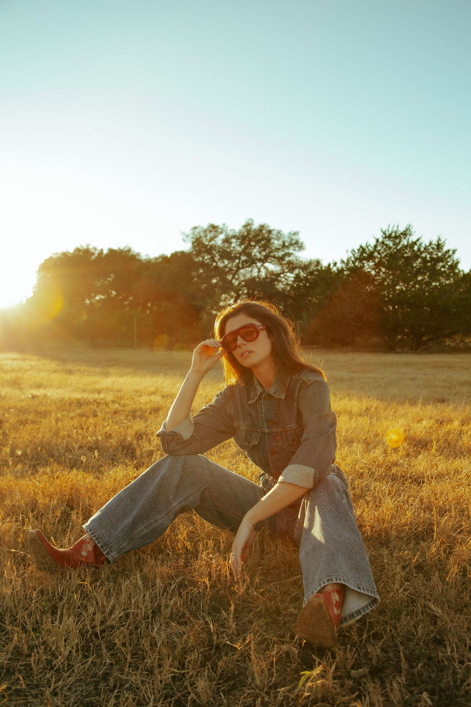 Retro-inspired fashion shoot in a sunlit field with denim and boots at sunset.