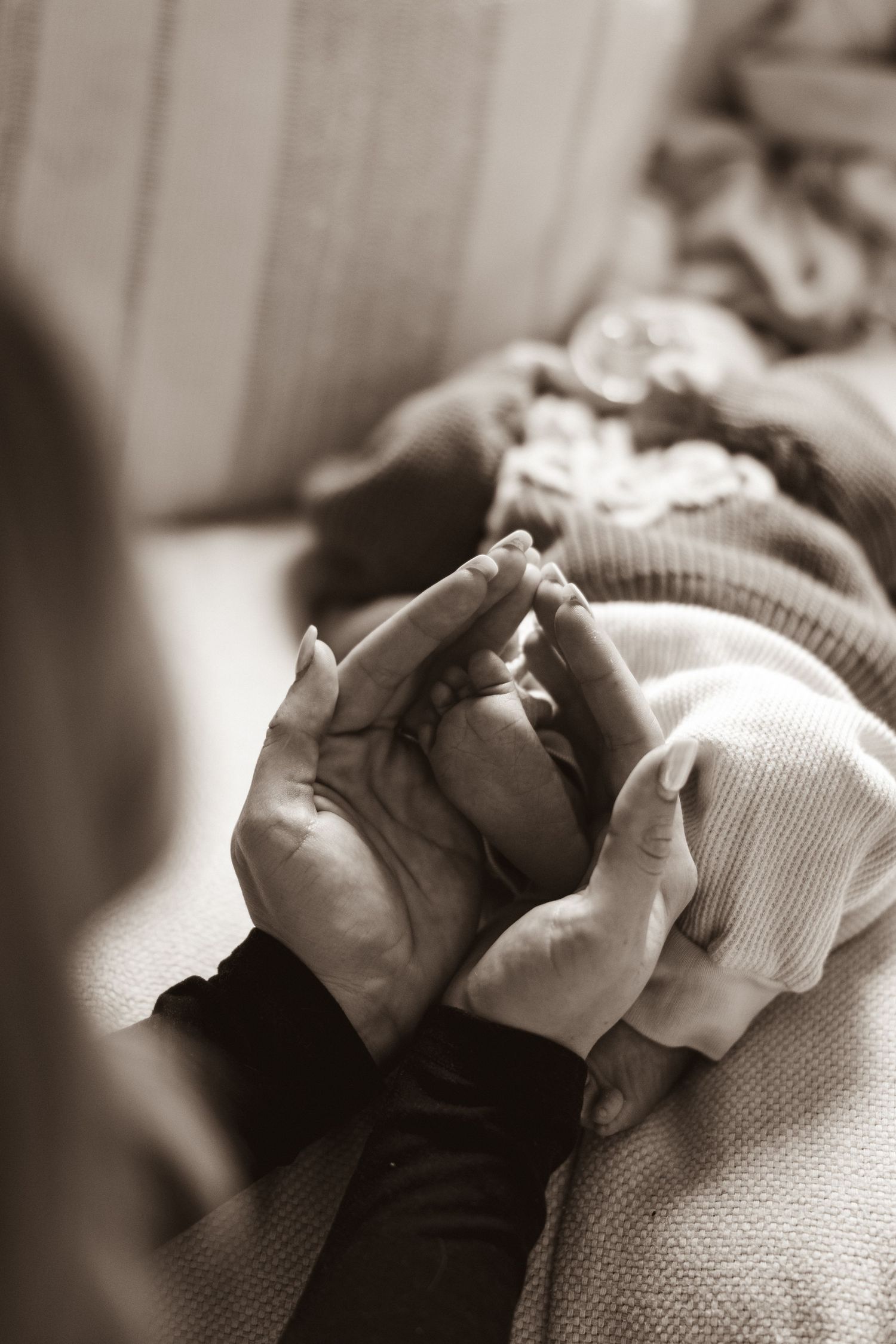 Close-up black and white image of a mother's hands gently holding her newborns foot.