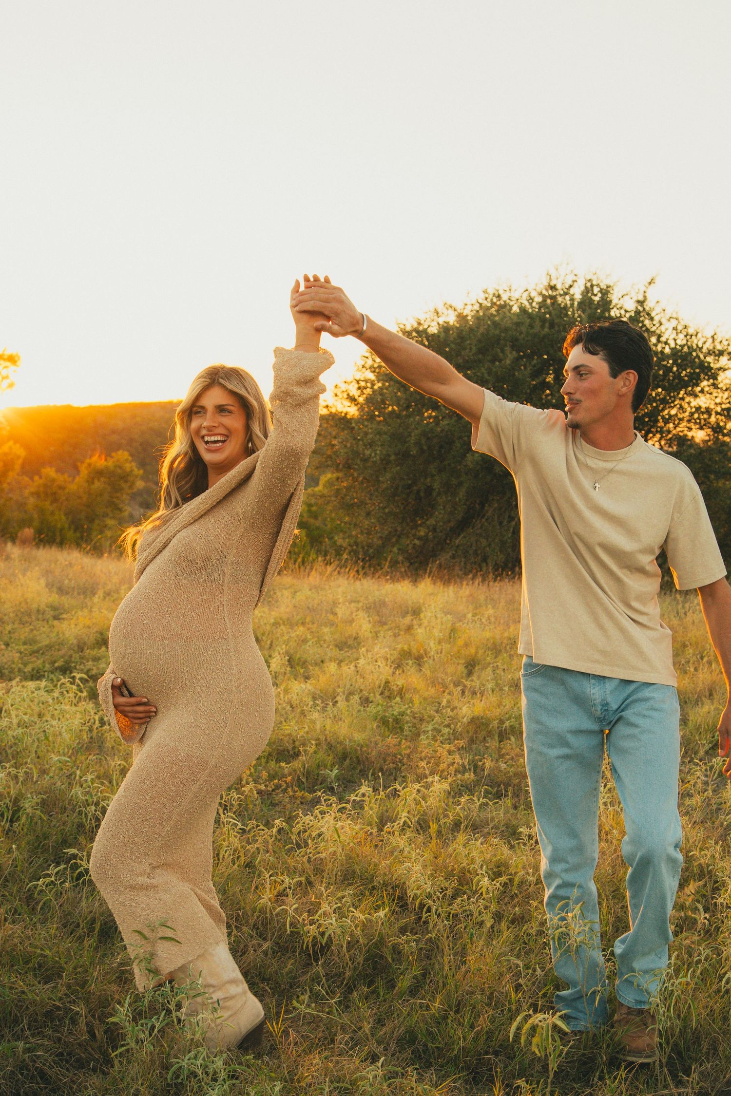 Joyful dancing moment during maternity photoshoot in a sunlit field.