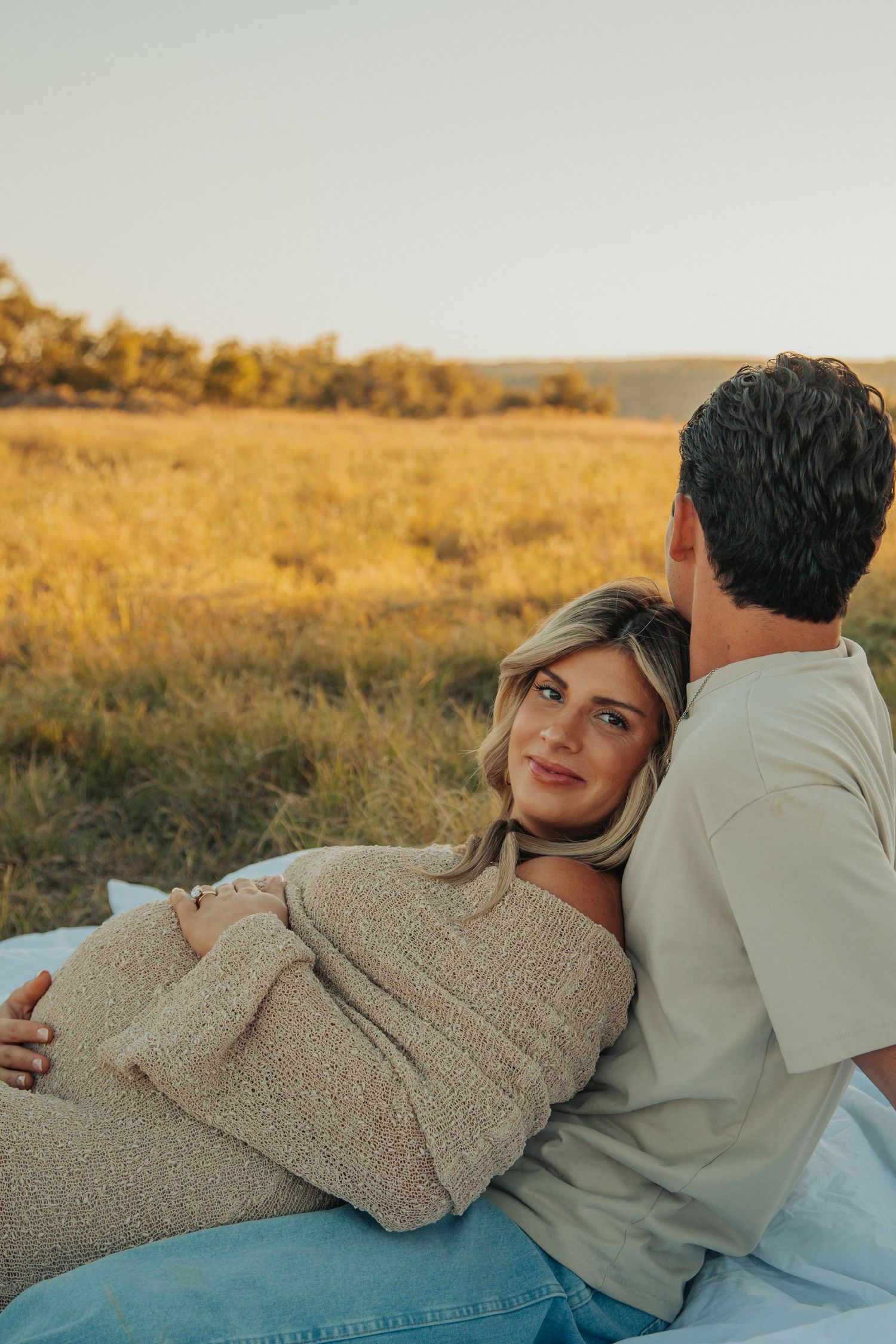 Couple relaxing on blanket in casual wear during golden hour maternity photoshoot.