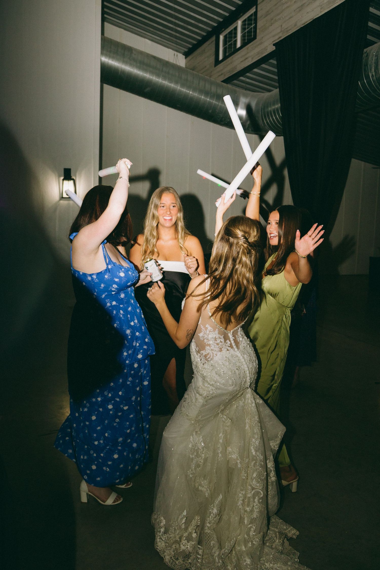 Wedding party dancing with glowing foam sticks in an indoor venue.
