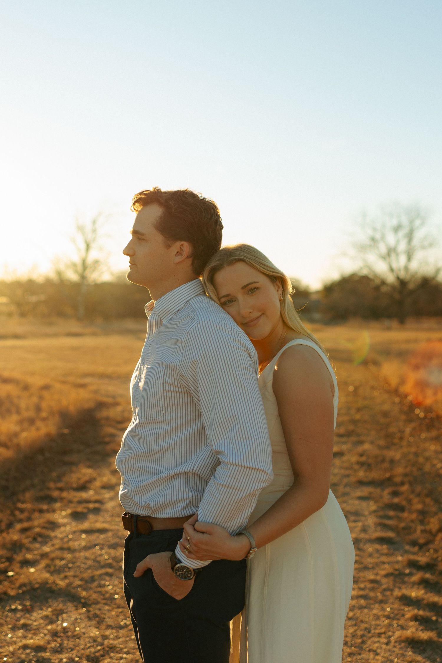 Couple embraces in a golden field during sunset, creating a romantic silhouette against the warm sky.