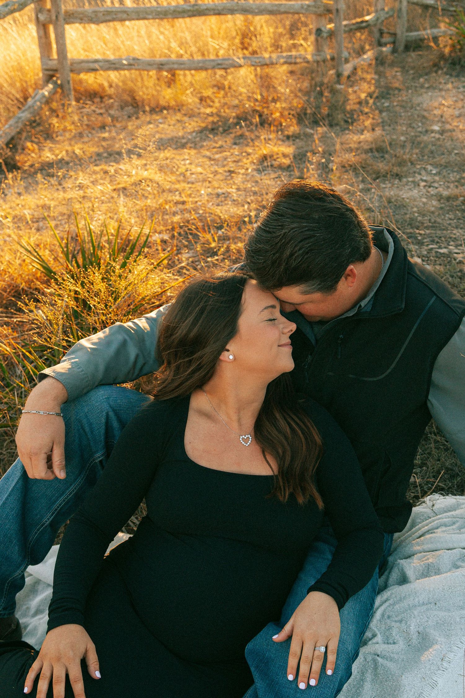 Romantic couple sharing intimate moments on blanket during golden hour maternity photoshoot.